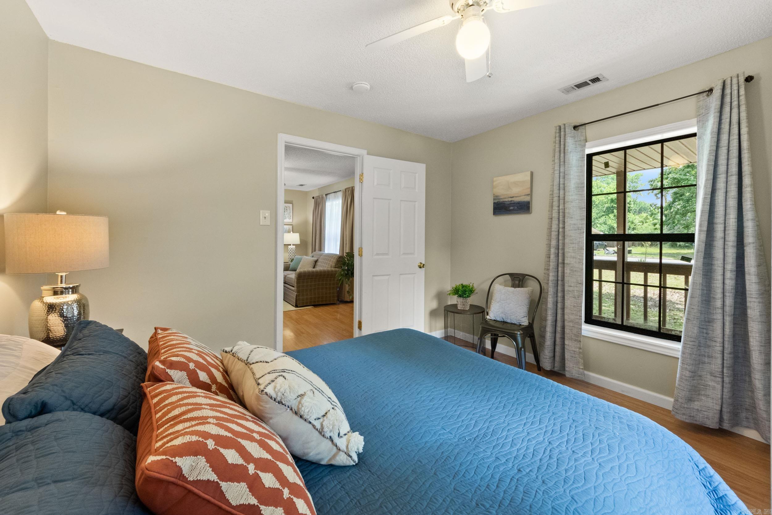 Furnished bedroom with a blue quilted bed and a large window overlooking a green yard.