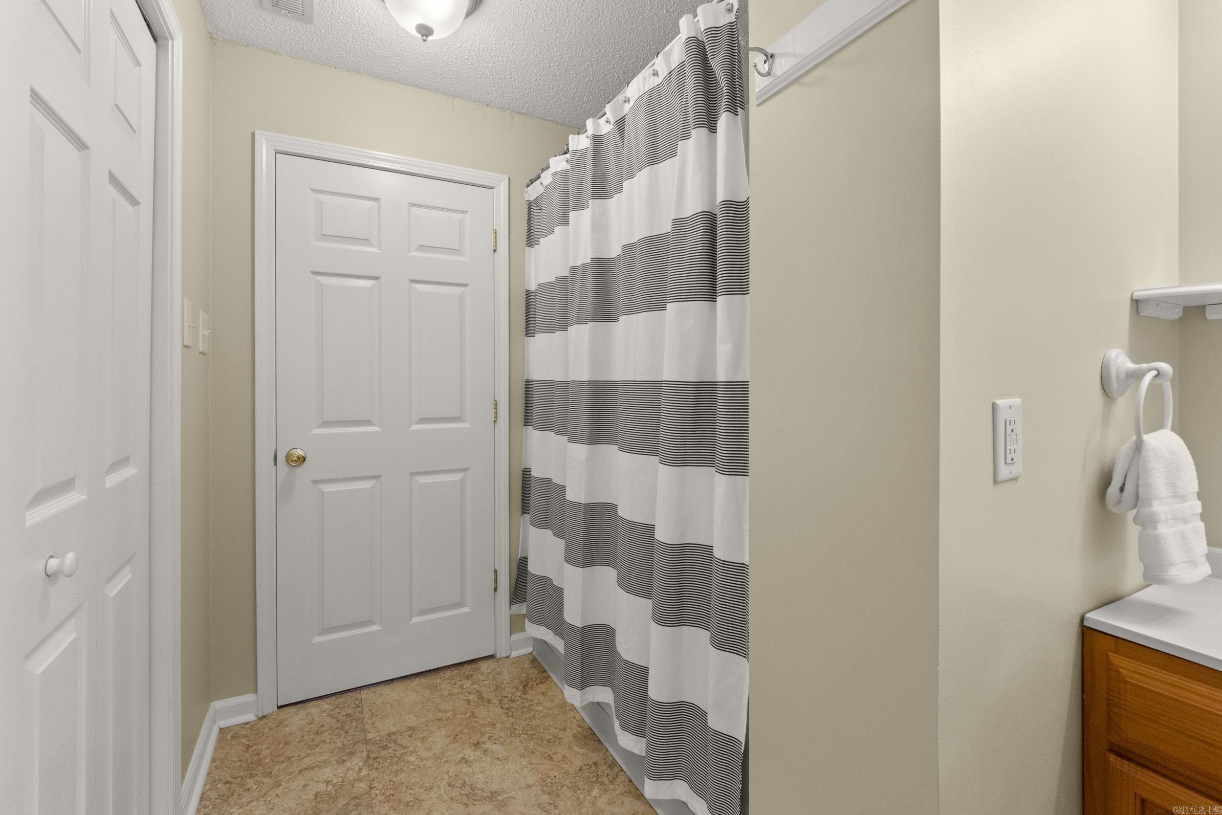 Bathroom with a black-and-white striped shower curtain and tan tile floor.