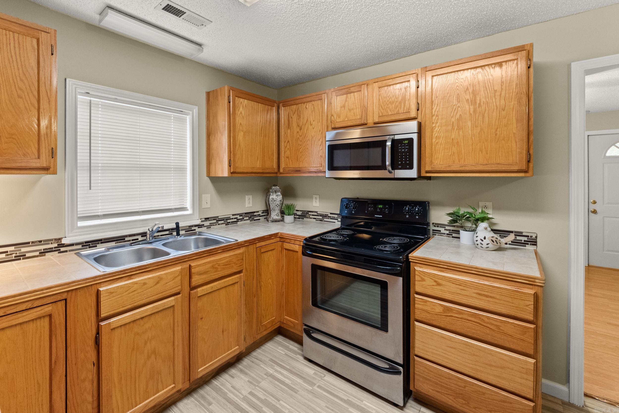 Kitchen with honey-colored cabinets, tiled counters, a double sink, and a black-and-stainless range.