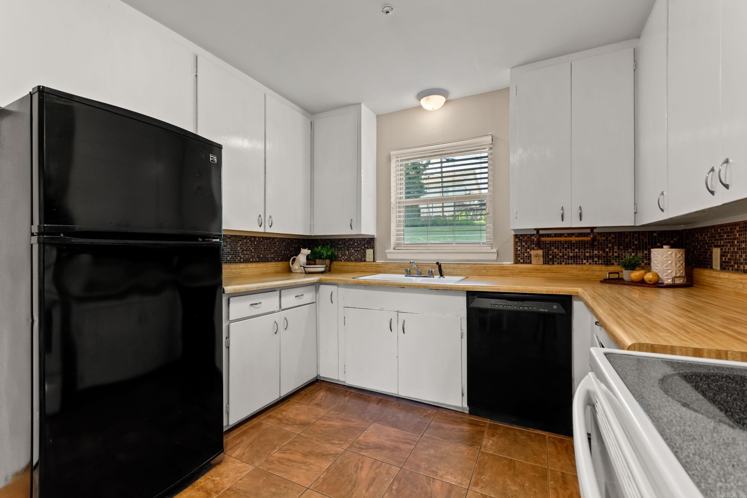 Kitchen with butcher-block counters, white cabinets, and dark mosaic backsplash.