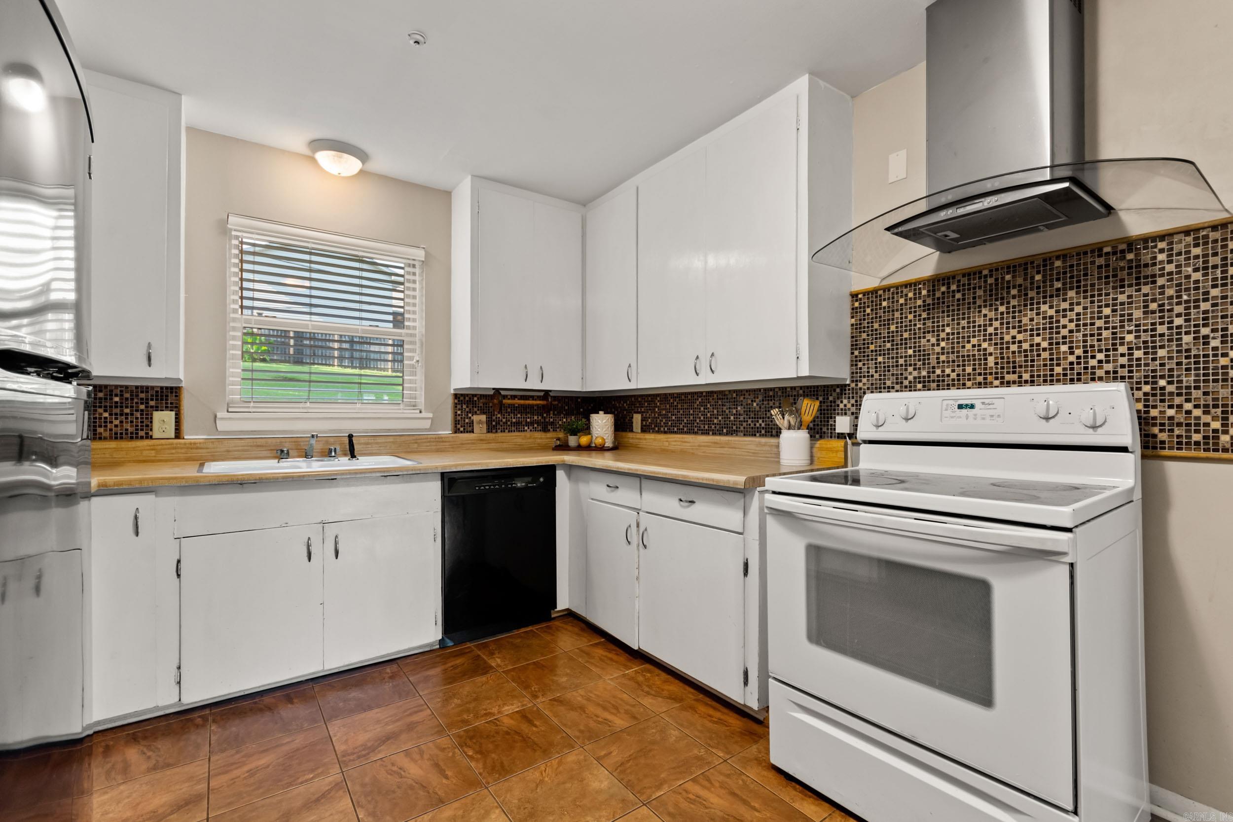 Kitchen with white cabinets, wood-look countertops, mosaic backsplash, and brown tile flooring.