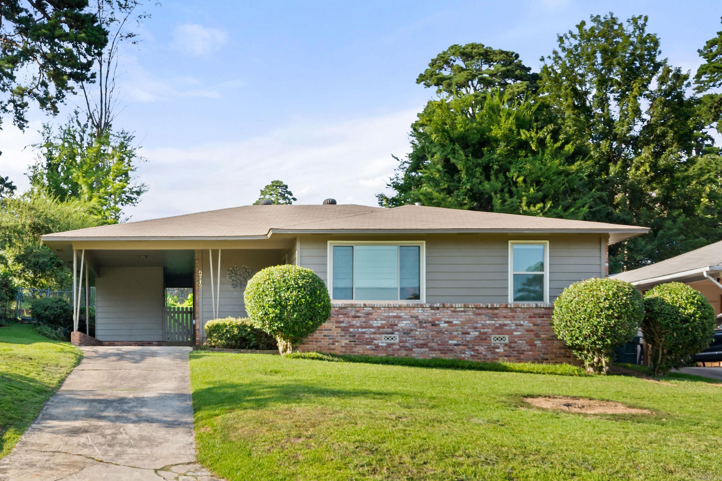 Single-story gray ranch home with a brick facade, covered entry, trimmed shrubs, and a concrete driveway.