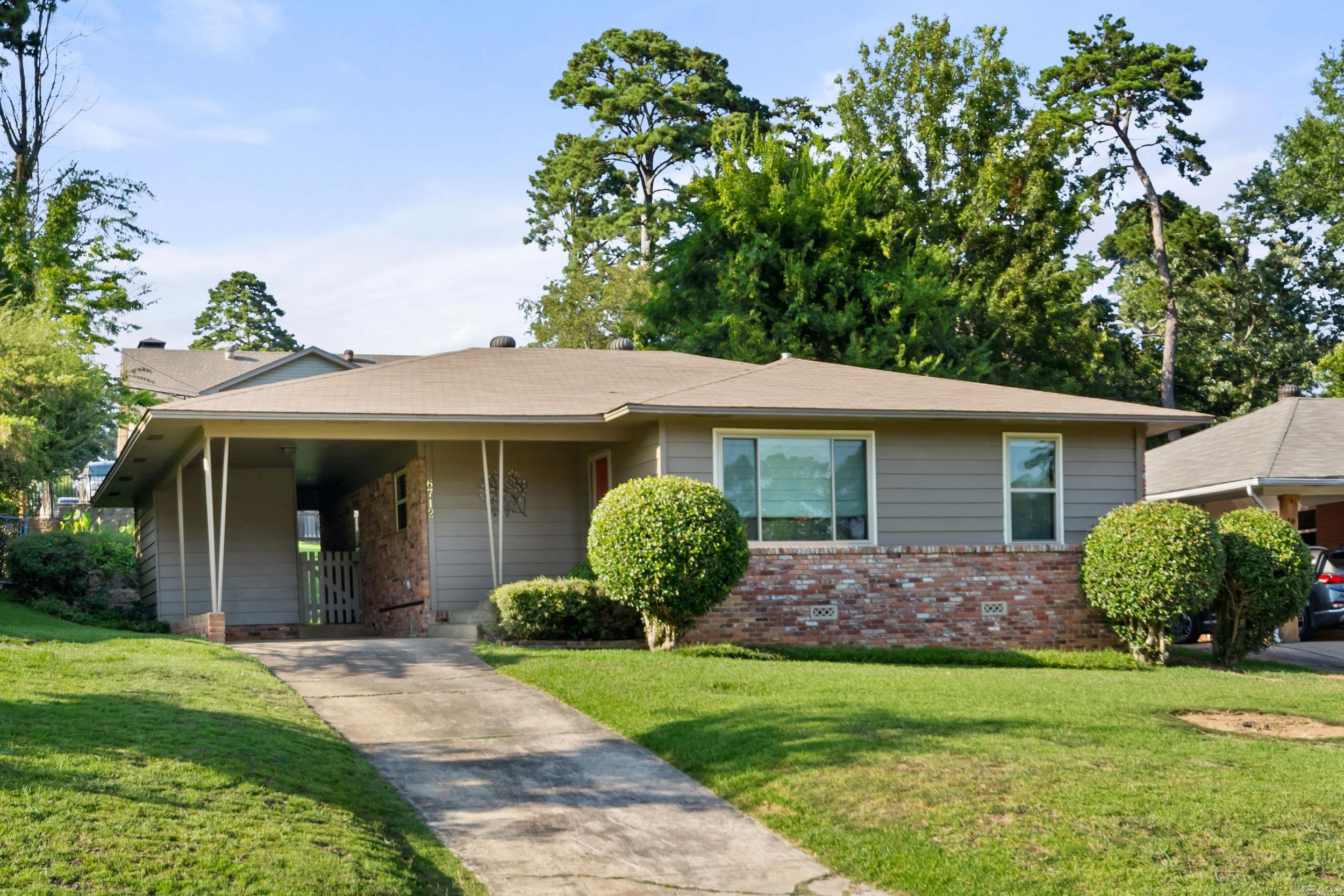 Single-story gray ranch house with brick facade, covered carport, trimmed shrubs, and front lawn.