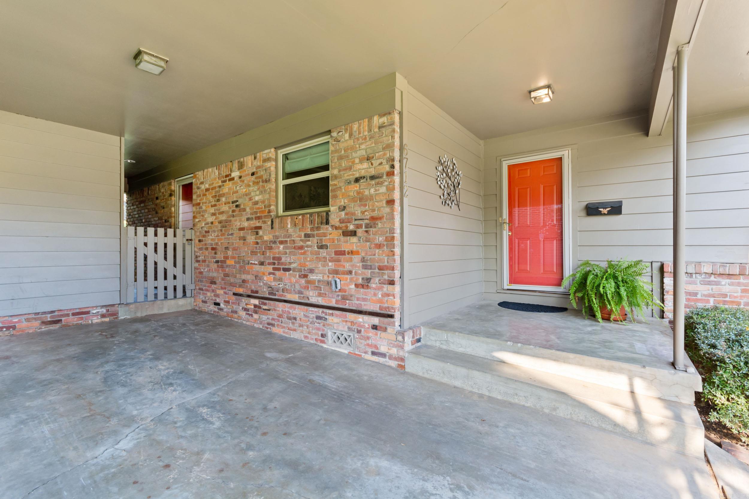 Covered brick-and-siding entry porch with a bright red front door and potted fern.