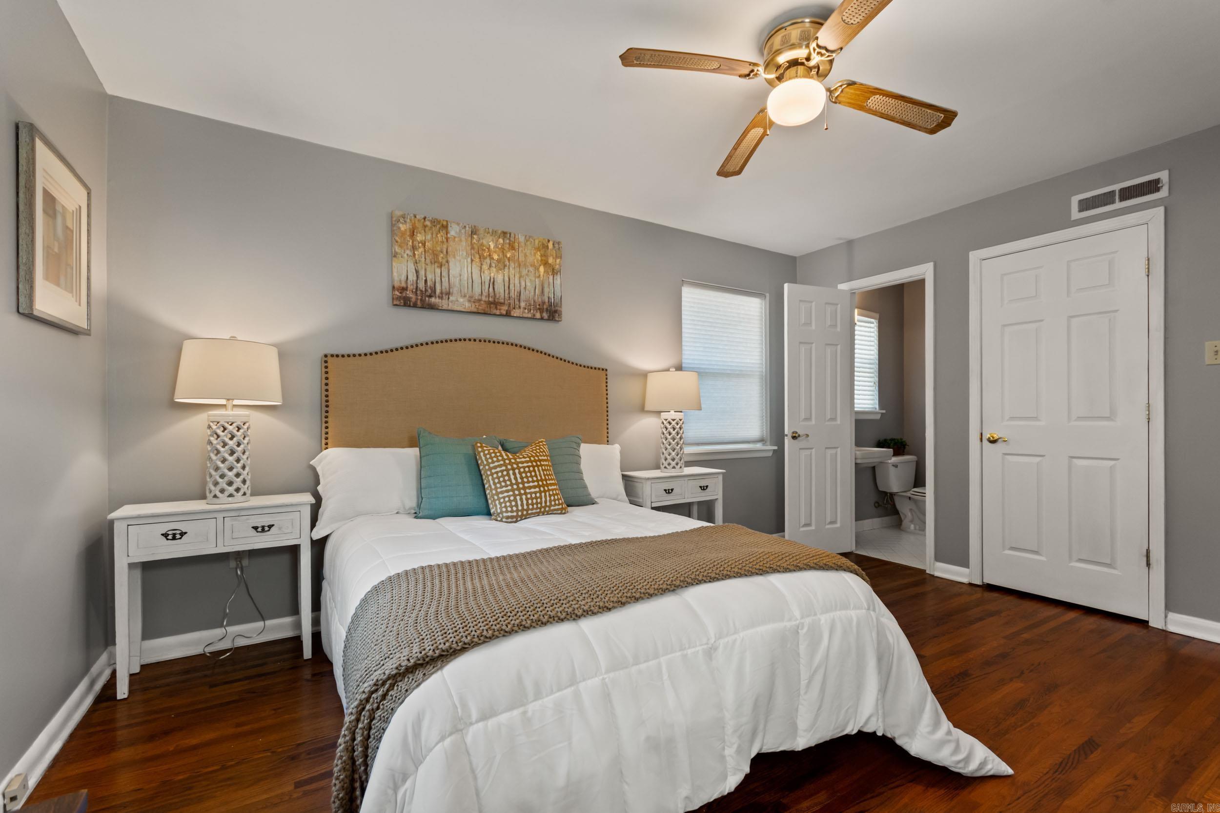 Bedroom with a white bed, tan headboard, dark hardwood floors, and an open doorway to the bathroom.
