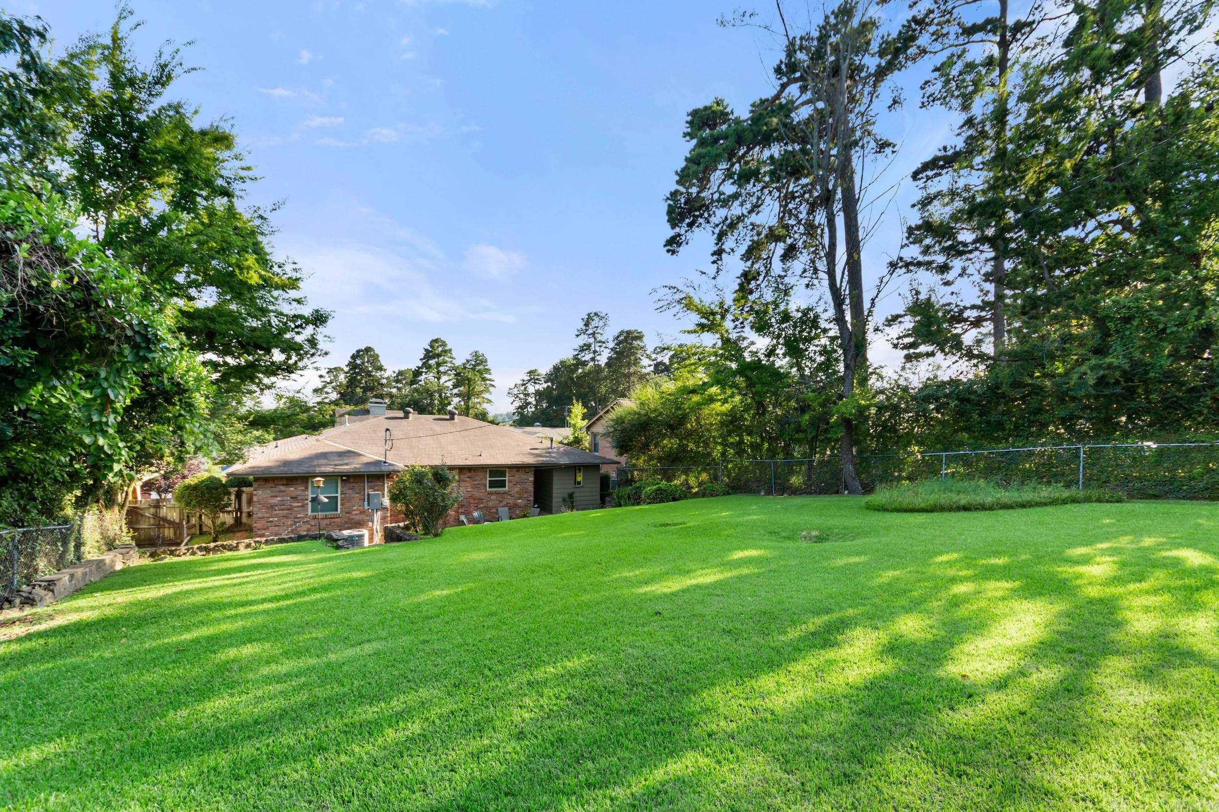 Brick house beyond a broad sloping lawn, shaded by mature trees.