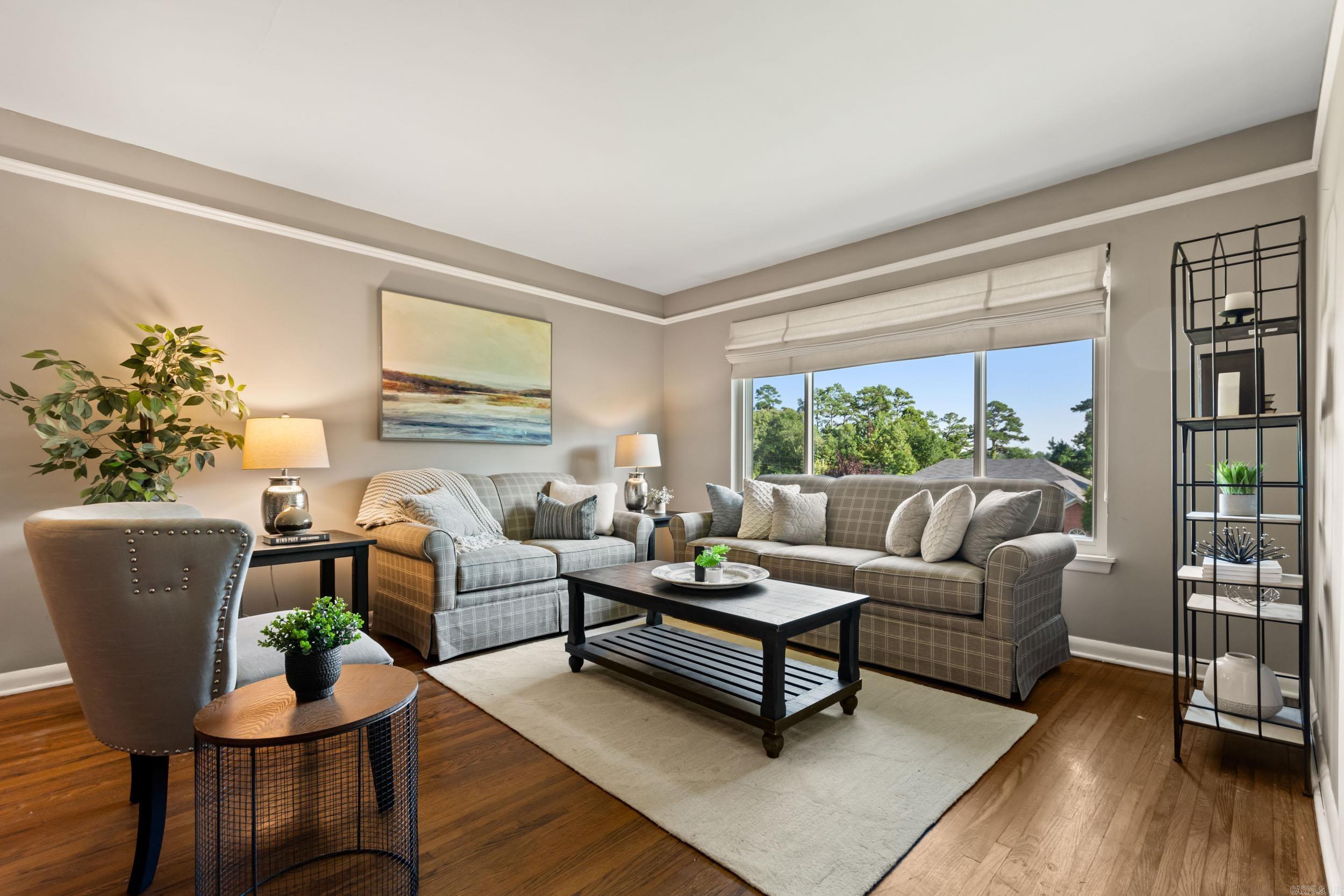 Staged living room with plaid sofas, hardwood floors, and a large window overlooking trees.