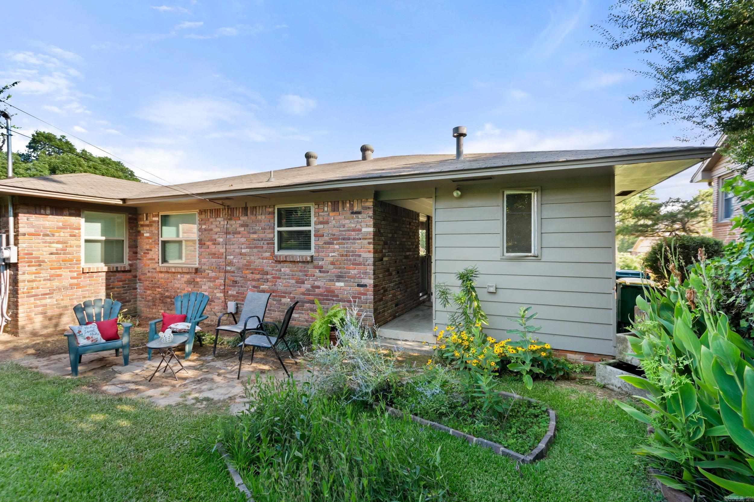 Rear of the brick-and-siding home with a covered entry, garden, and patio seating.