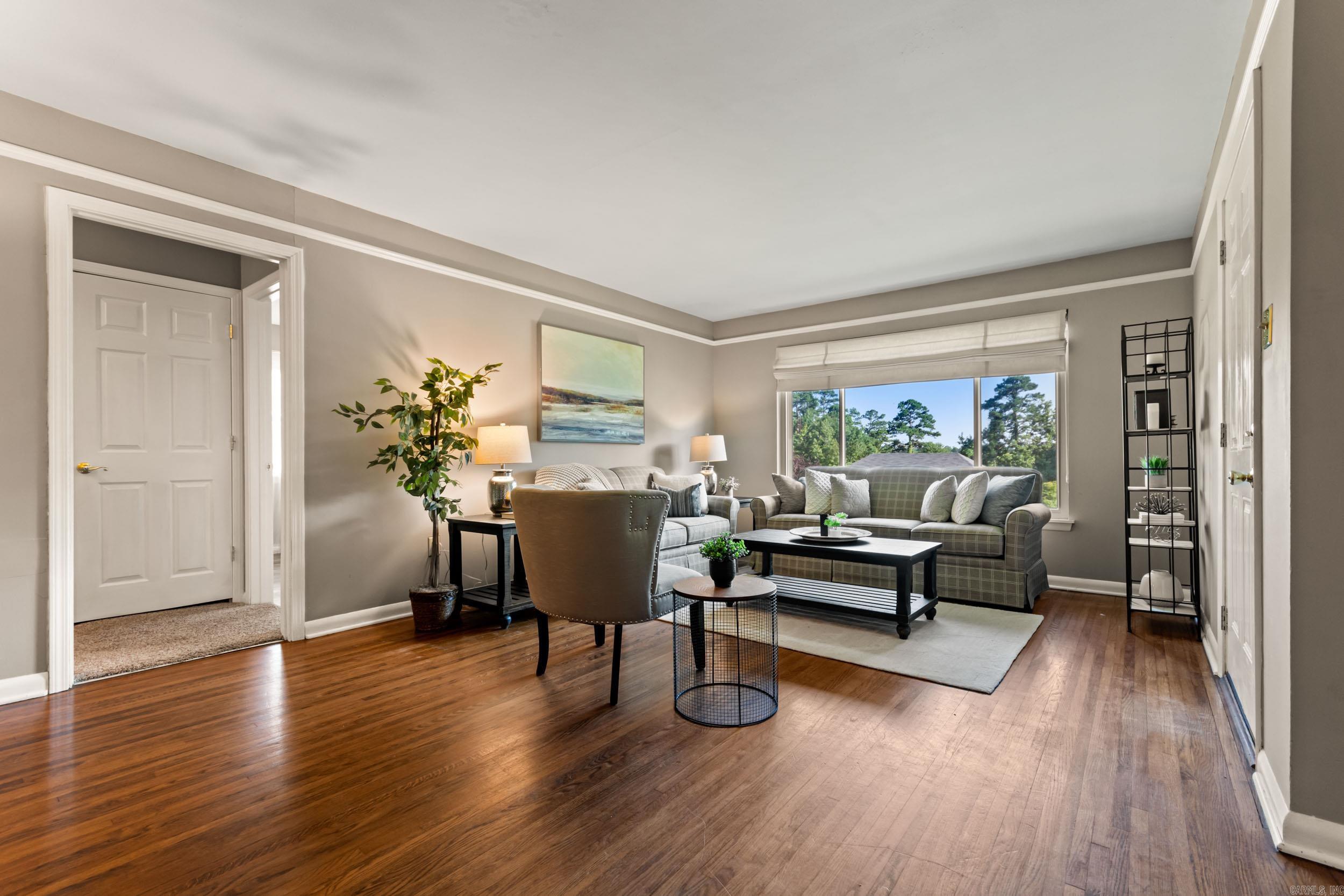 Living room with hardwood floors, gray seating, and a large window overlooking trees.