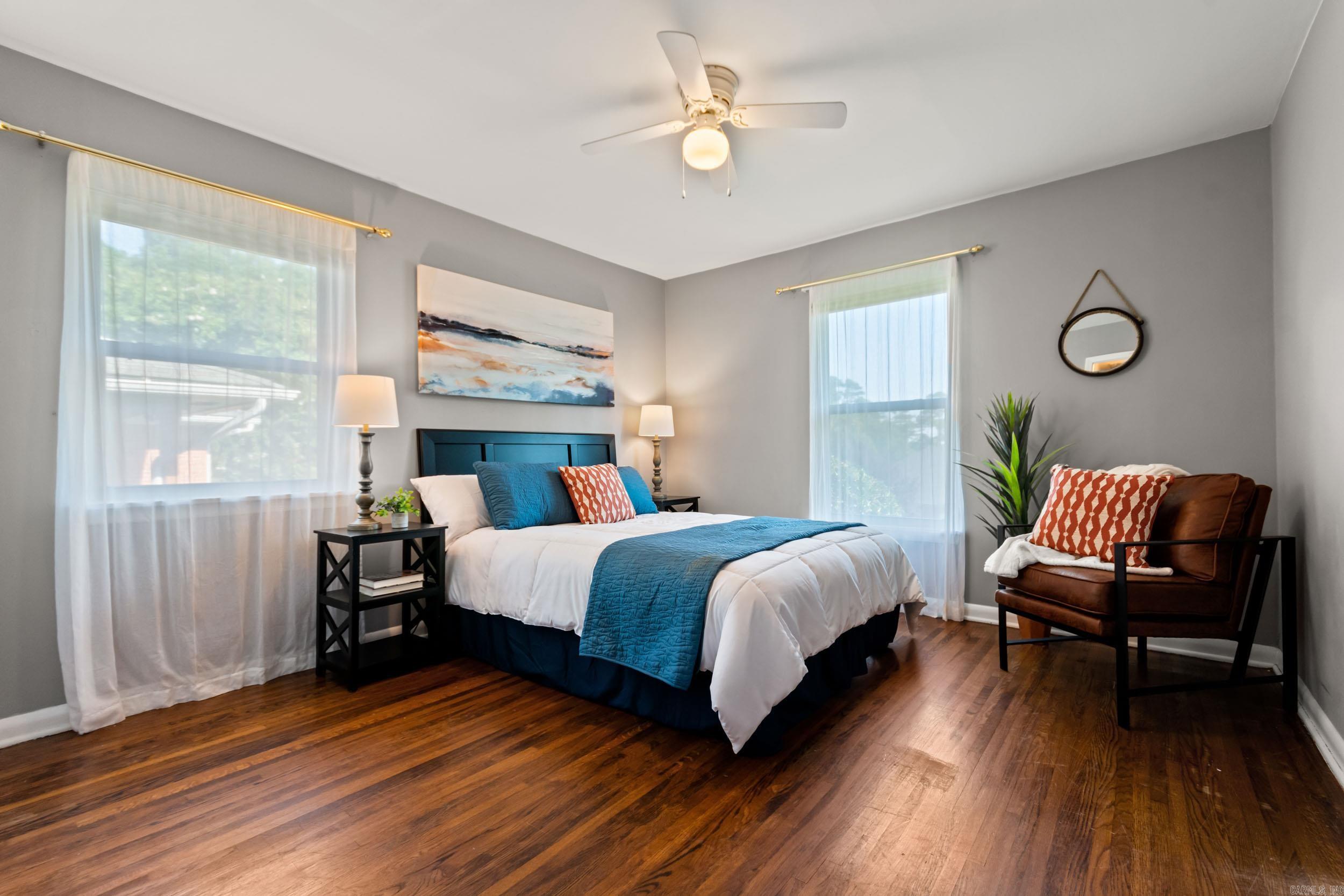 Staged bedroom with a blue-and-white bed, hardwood floors, and a brown leather armchair.