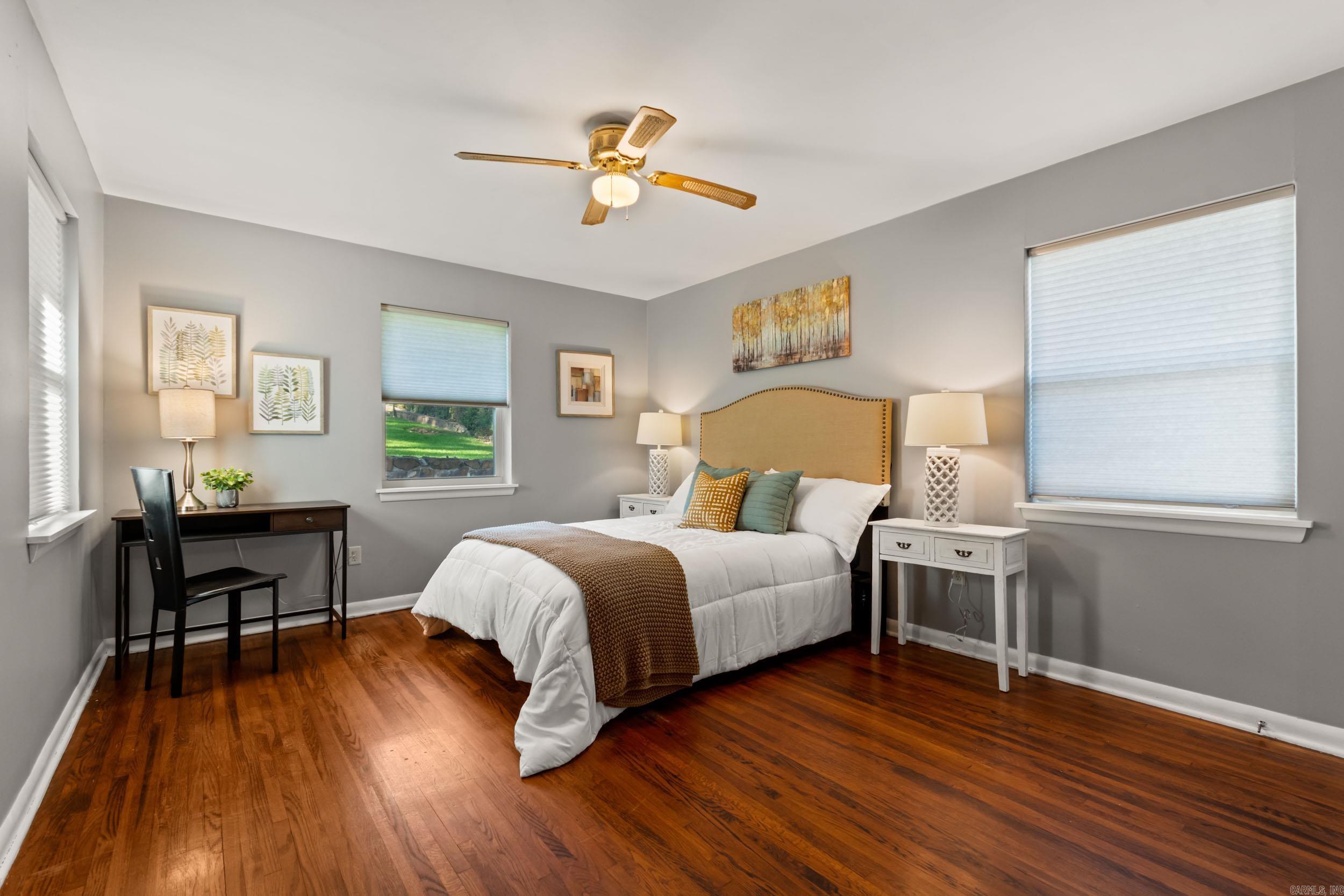 Bedroom with a white bed, tan upholstered headboard, hardwood floors, and a desk beside the window.