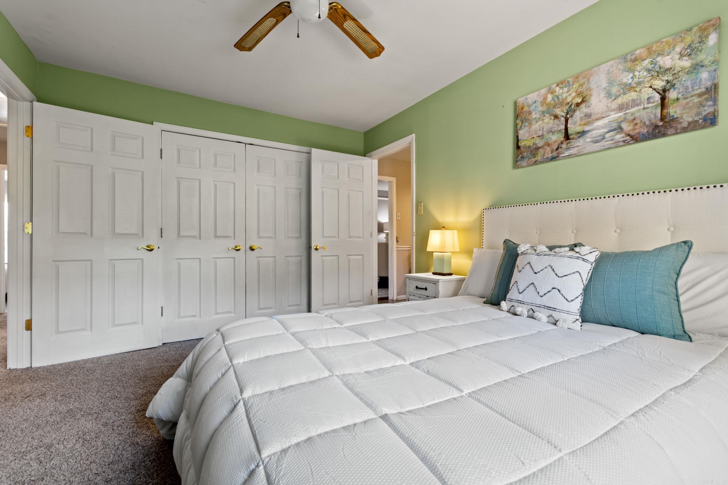 Bedroom with green walls, a white bed, teal pillows, and paneled closet doors.