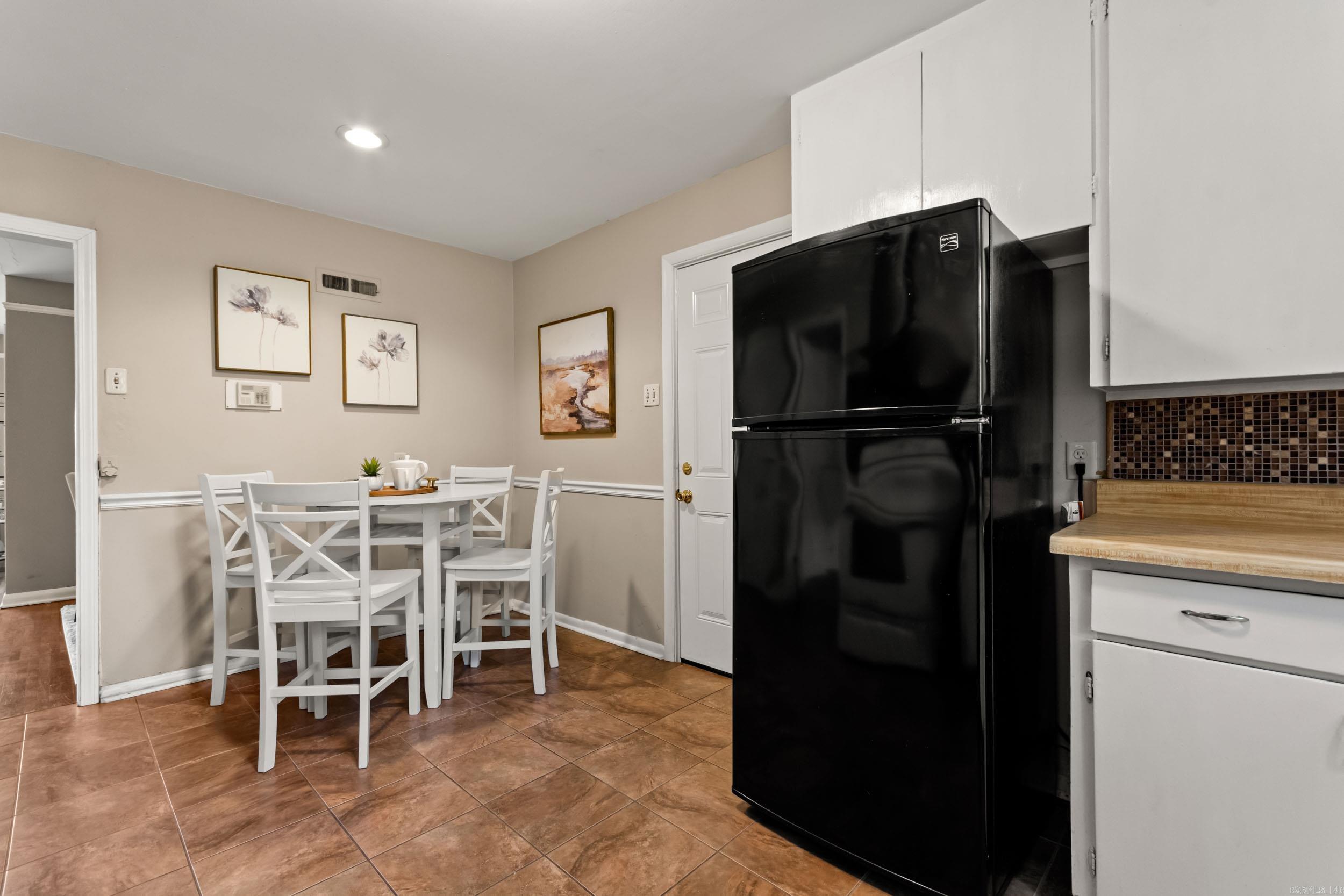 Kitchen dining area with a white table and chairs beside a large black refrigerator.