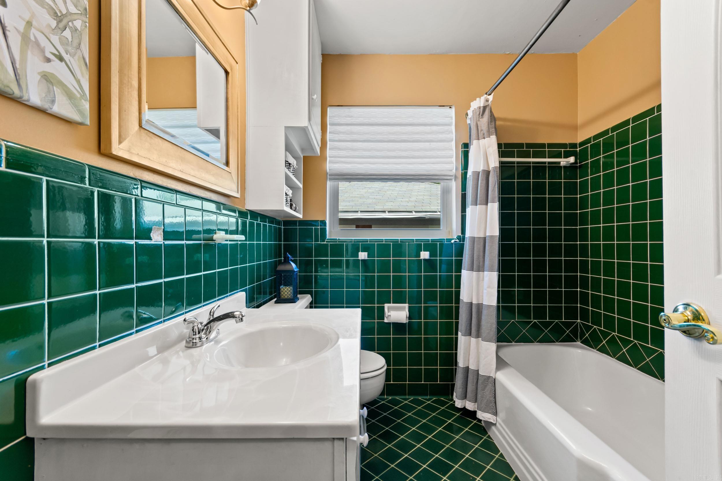 Bathroom with glossy green tile, white bathtub and vanity, and a striped shower curtain.