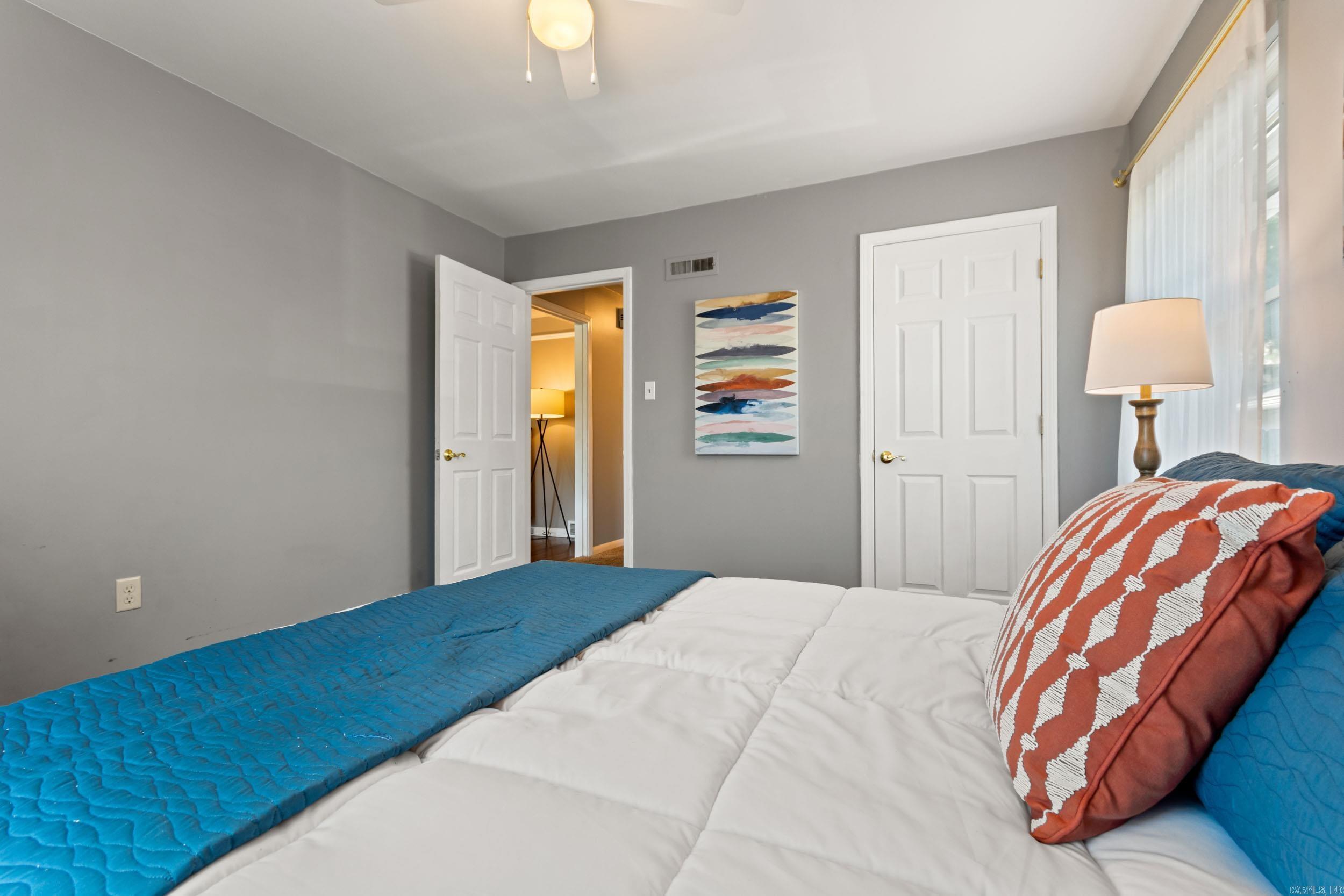 Bedroom with gray walls, blue bedding, white doors, and a colorful abstract wall painting.