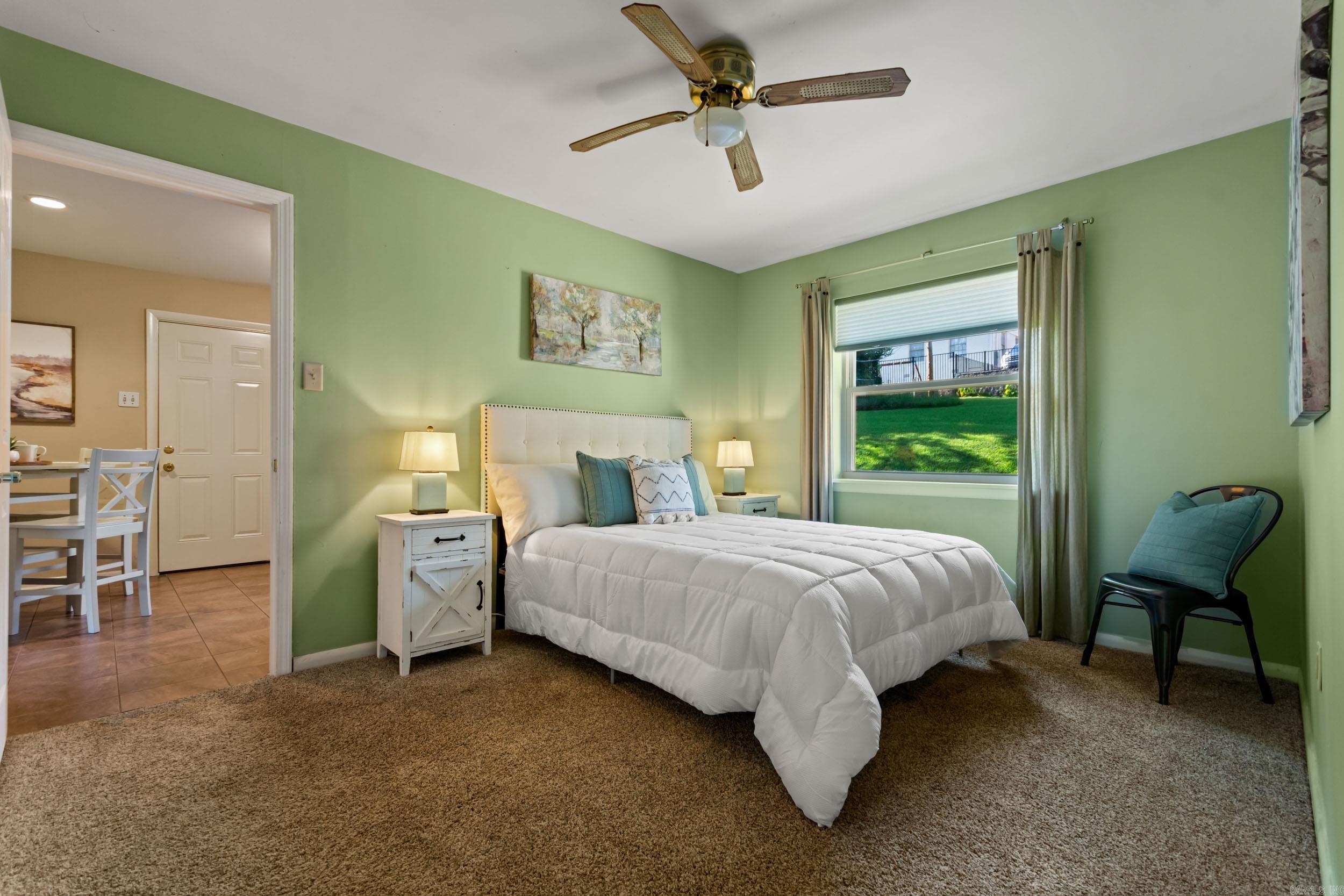 Staged bedroom with green walls, a white bed, and a window overlooking a grassy yard.