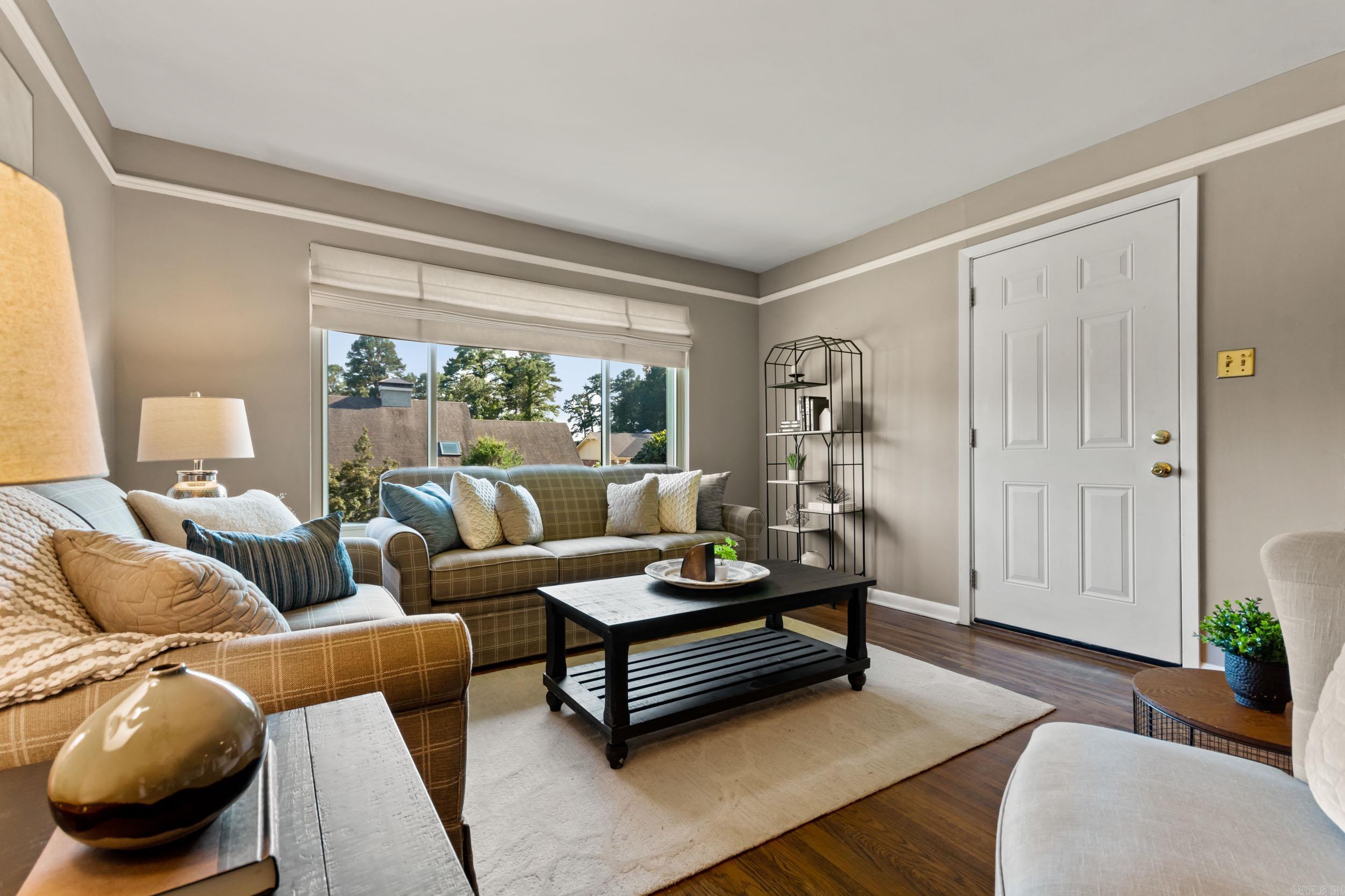 Furnished living room with plaid sofas, a black coffee table, and a large window overlooking trees.