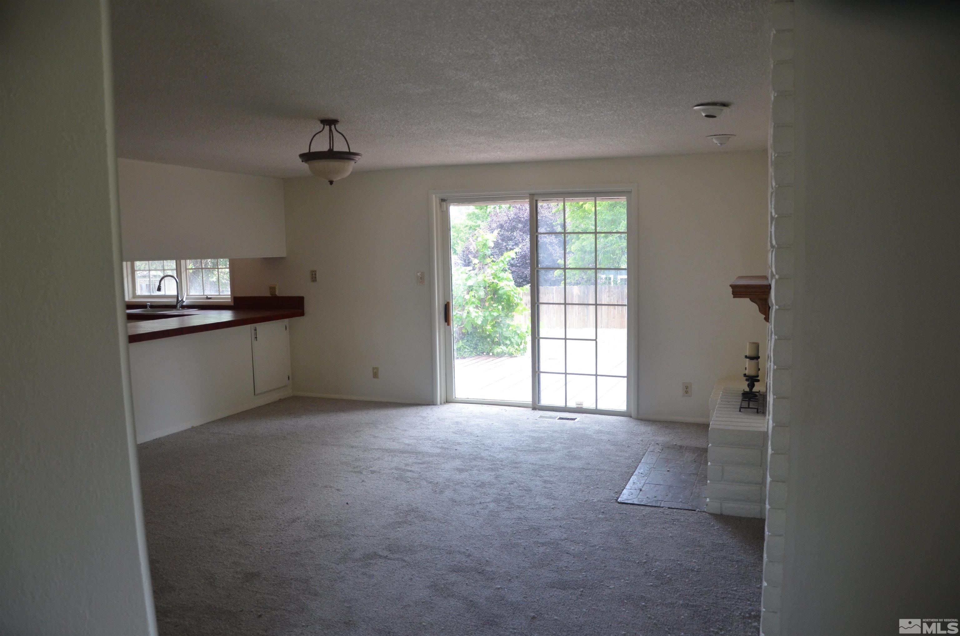 Empty carpeted living room with a white brick fireplace and sliding glass door to a patio.