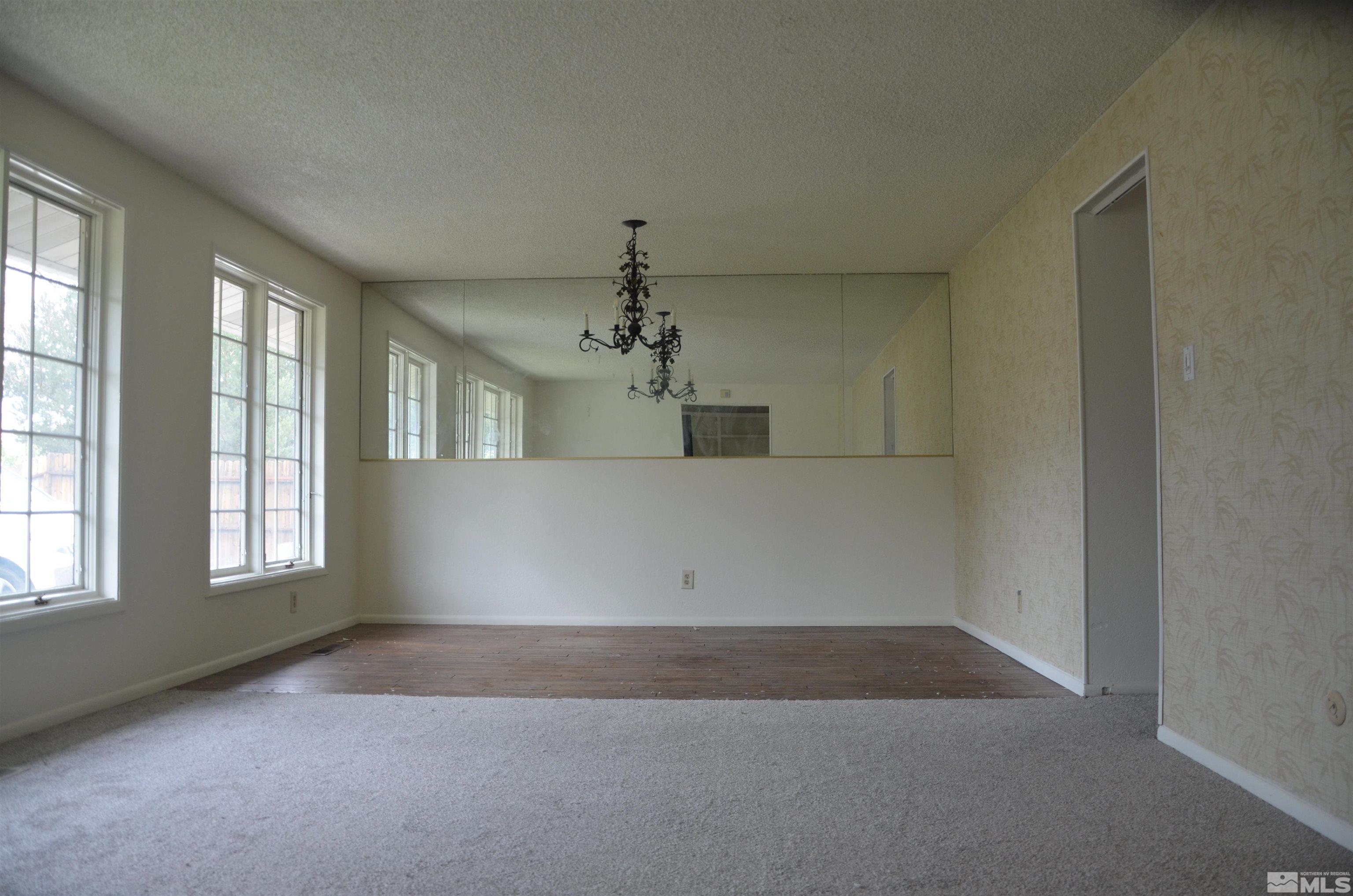 Empty dining room with mirrored wall, ornate chandelier, and tall windows.