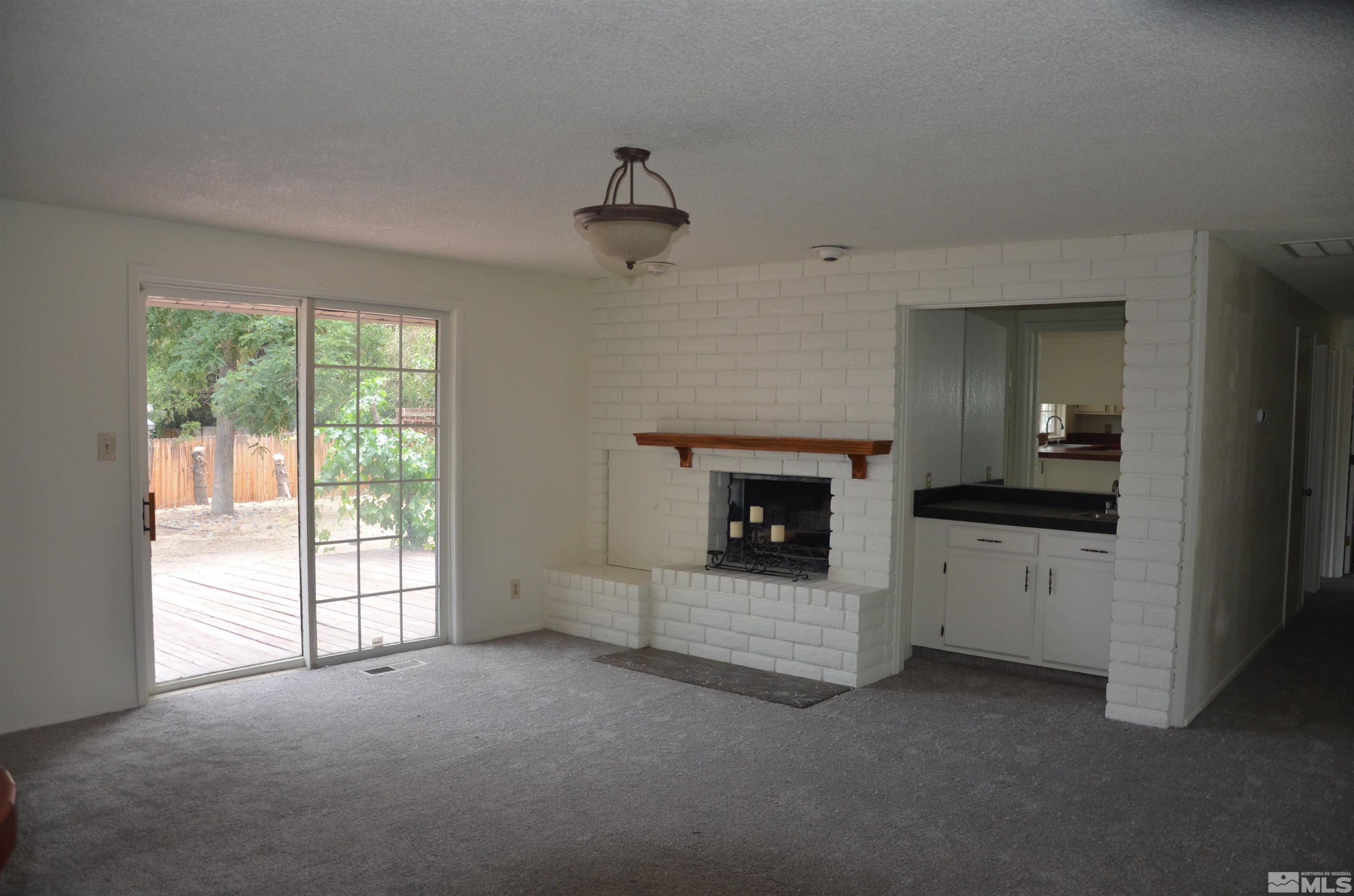 Empty living room with a white brick fireplace and sliding glass doors to a deck.