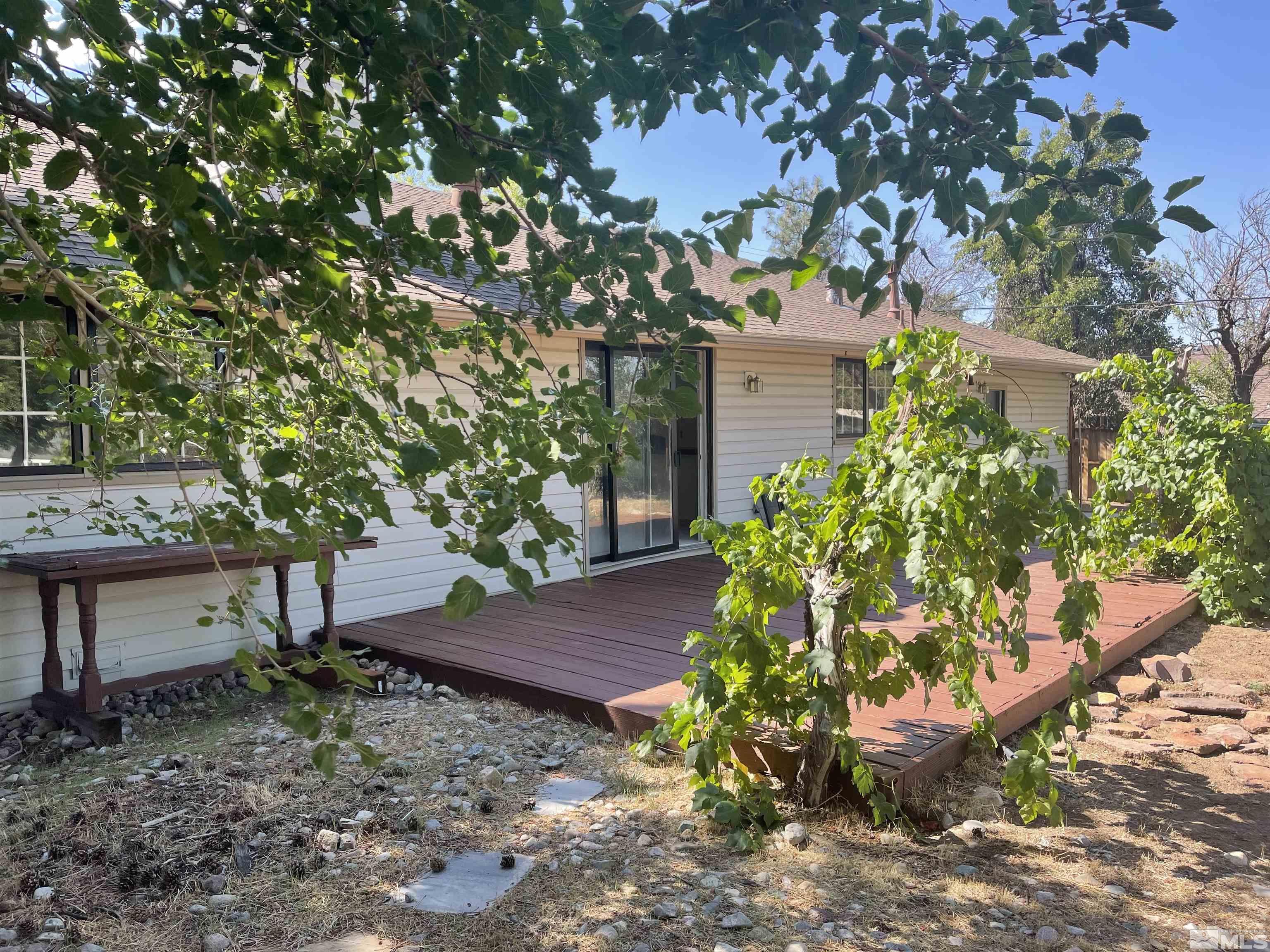 House exterior with a broad wooden deck, sliding glass door, and leafy yard.