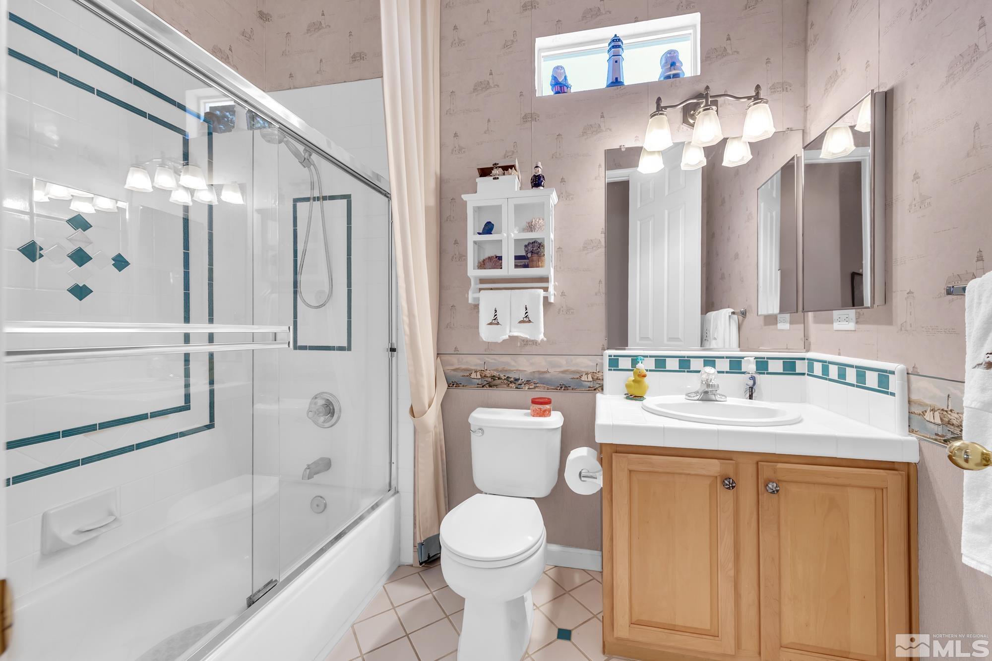 Bathroom with glass-enclosed shower and tub, teal tile accents, and a wood vanity.