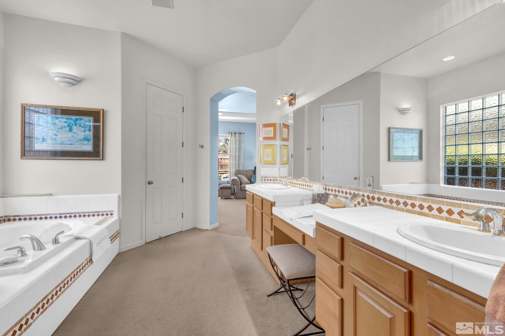 Bathroom with twin tiled vanities, warm wood cabinetry, a built-in tub, and a glass-block window.