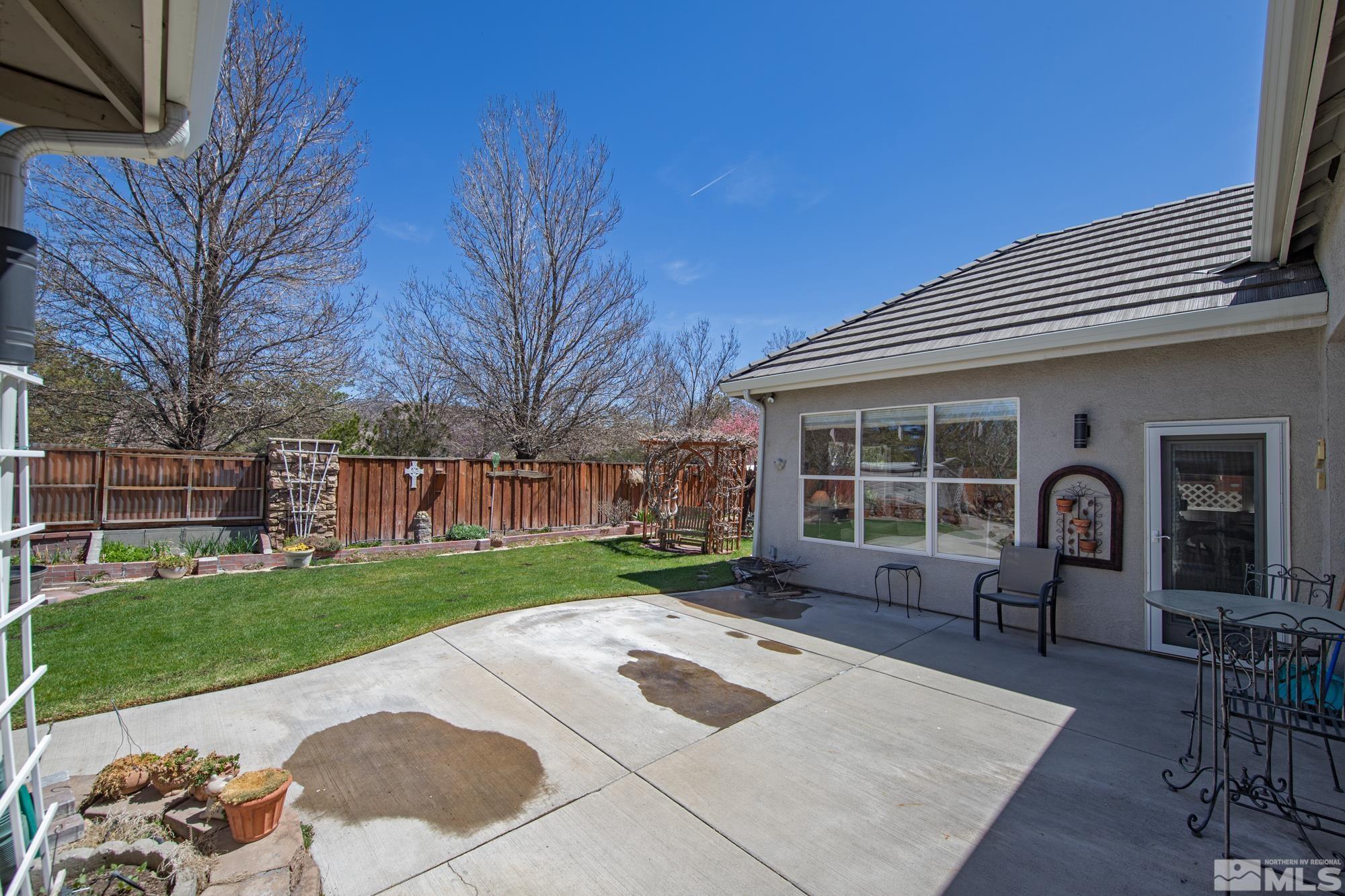 Backyard patio with outdoor dining furniture, a fenced lawn, and raised garden beds.