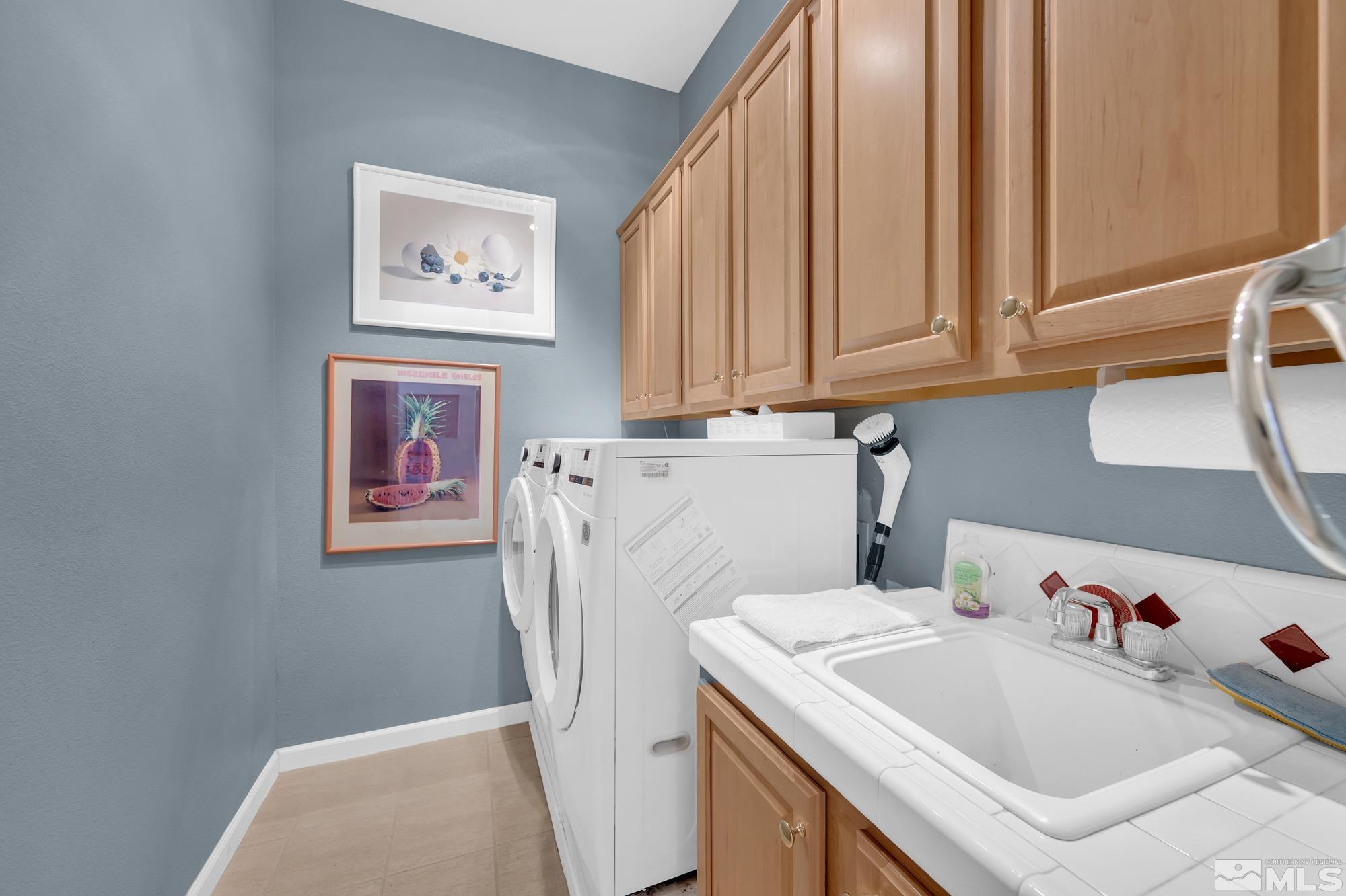 Laundry room with front-loading washer and dryer, utility sink, and light wood cabinets.