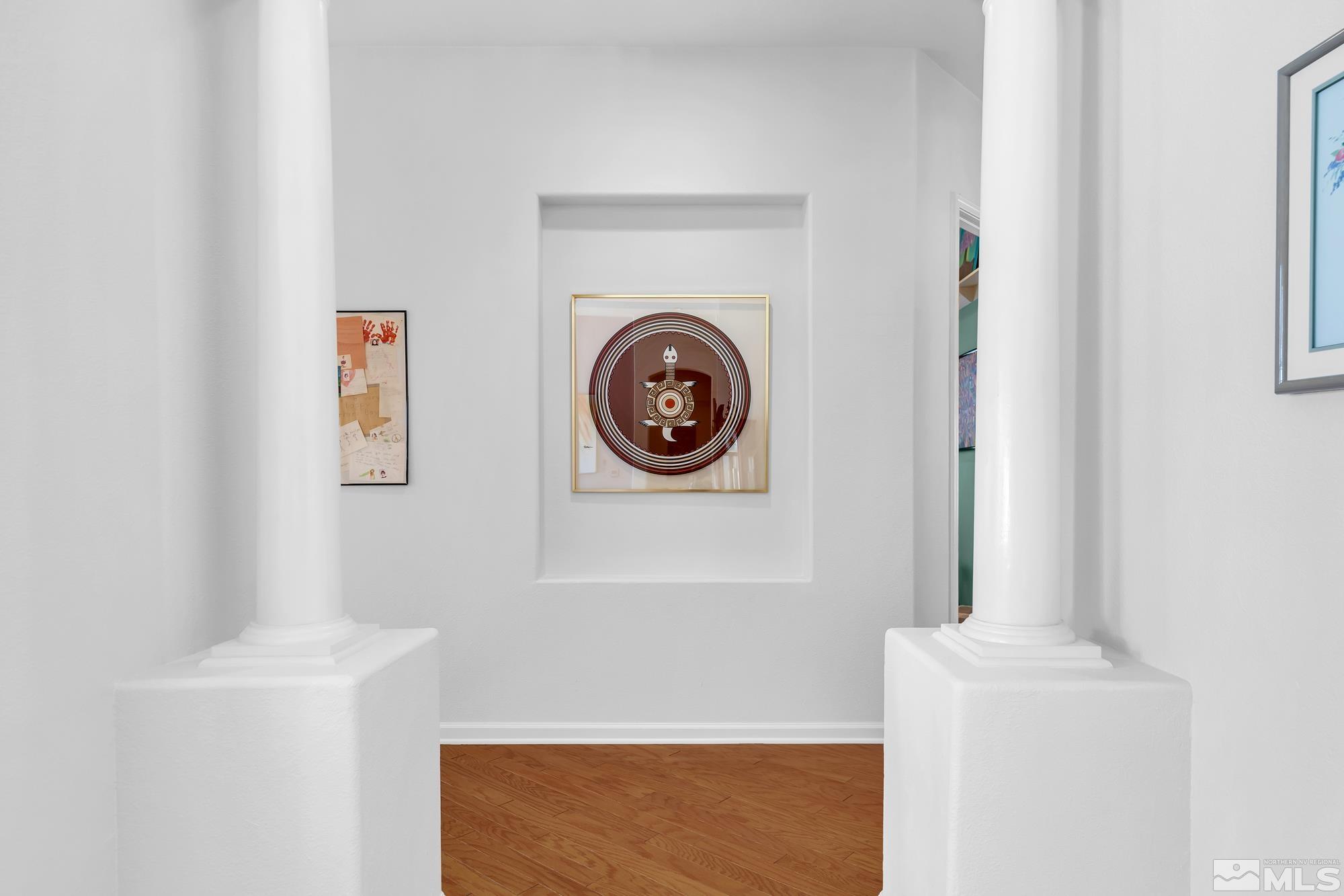 Bright white hallway framed by columns, with a recessed art niche and warm hardwood flooring.