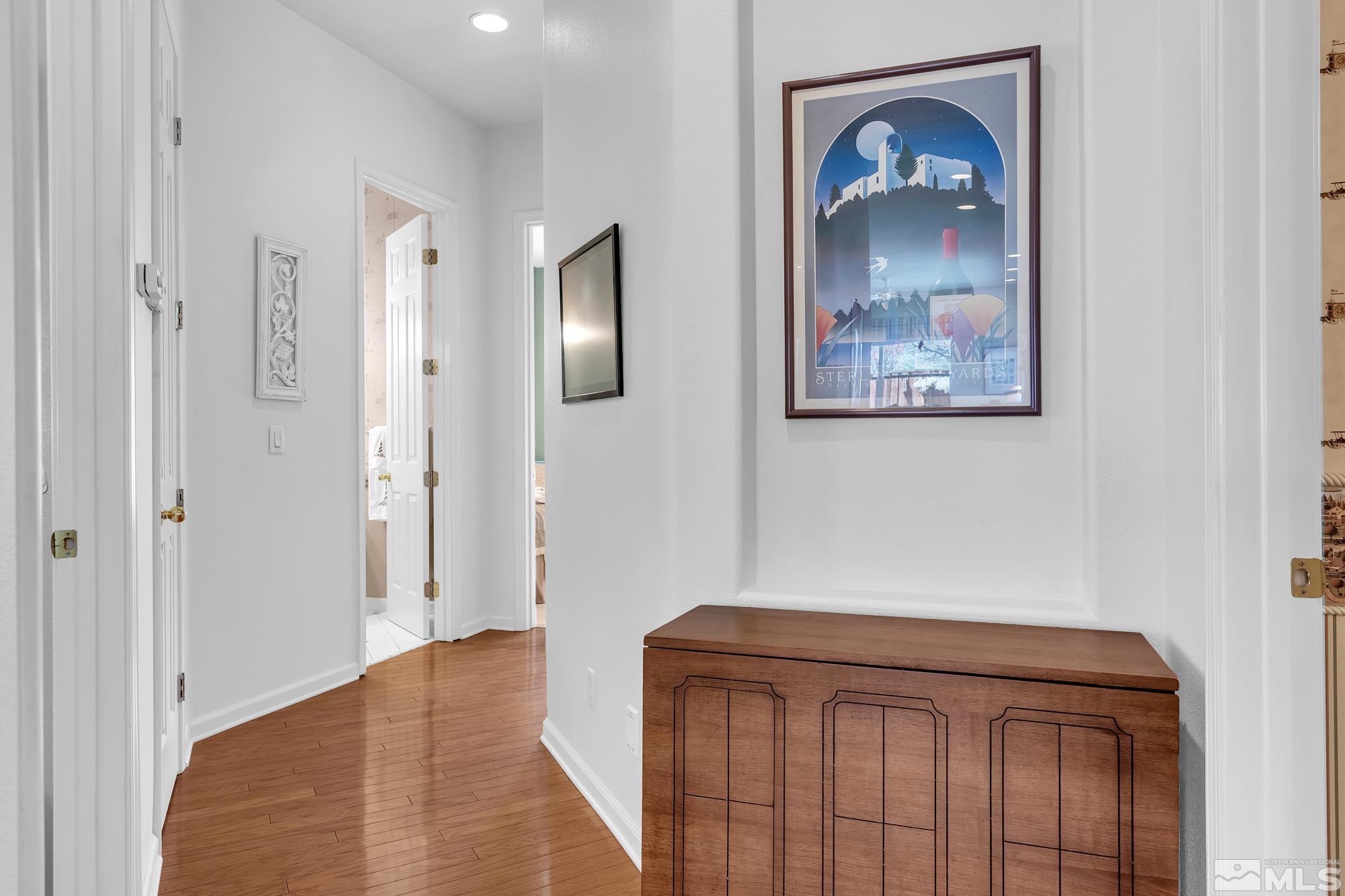 Bright hallway with hardwood floors, open doorways, and a wooden console cabinet beneath framed artwork.
