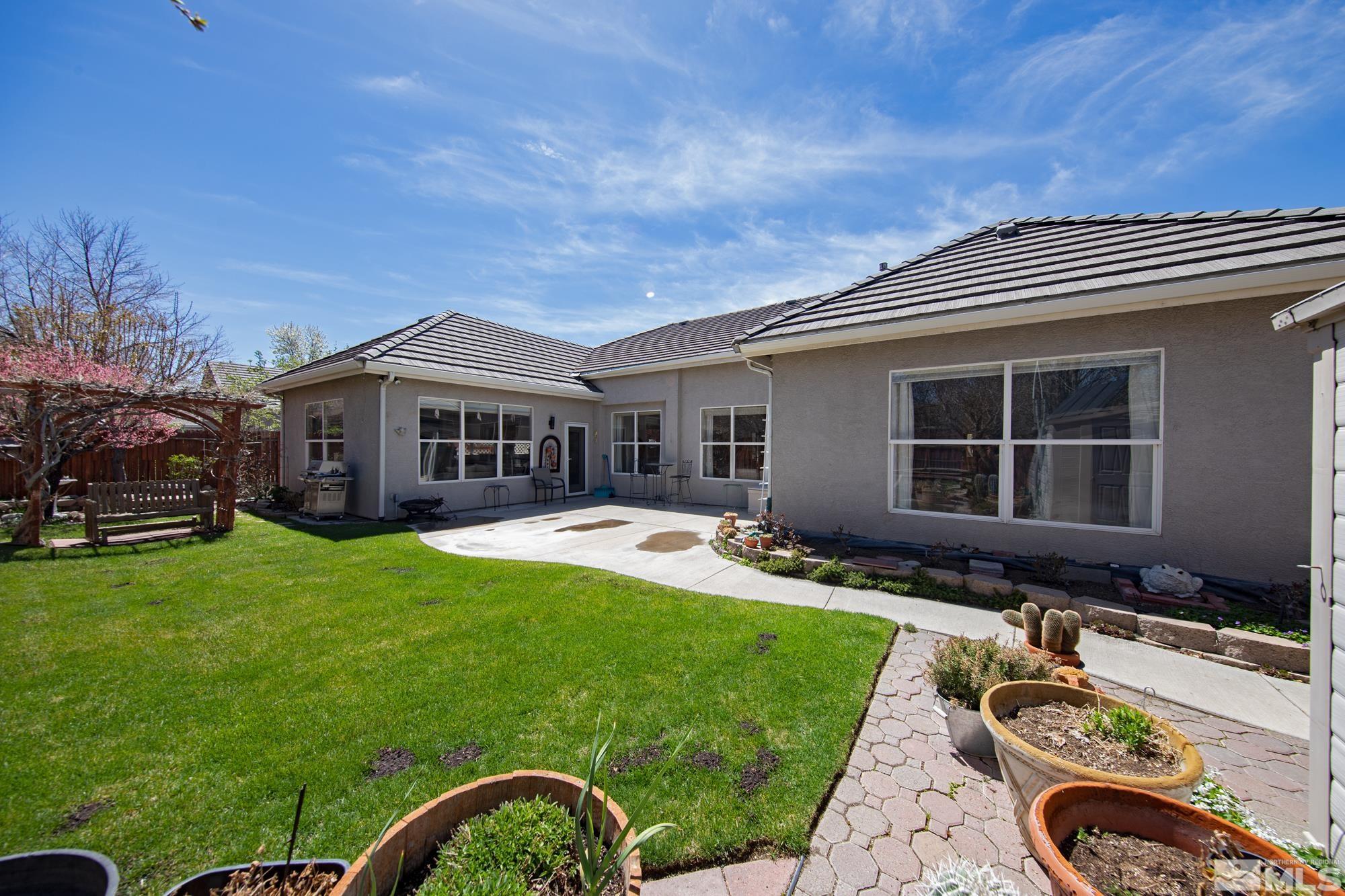 Home’s backyard with a broad lawn, concrete patio, raised planters, and a wooden arbor.