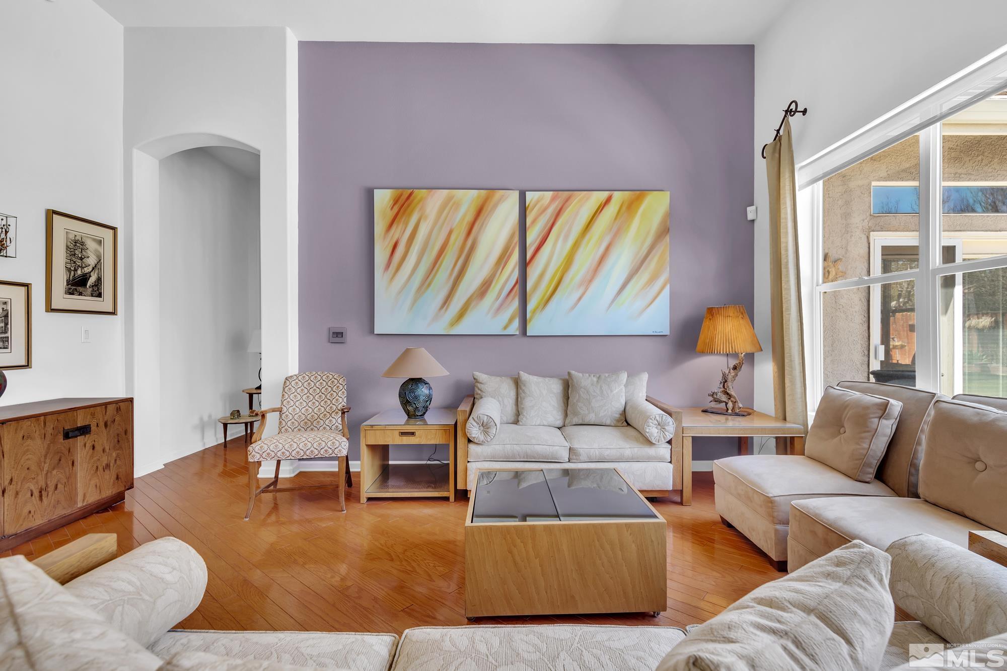 Living room with cream sofas, a lavender accent wall, hardwood floors, and large abstract artwork.