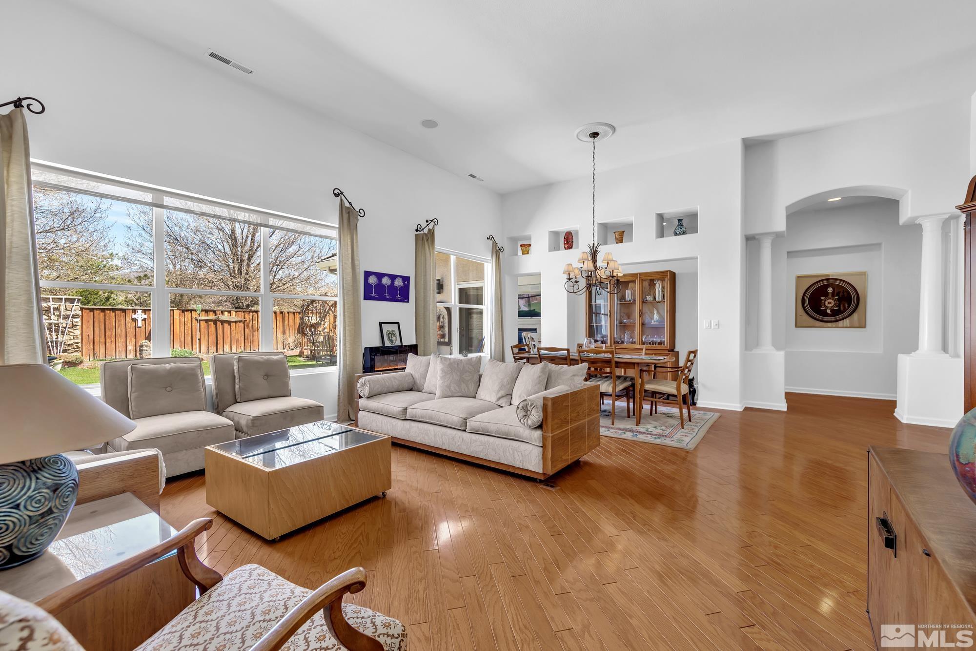 Open-plan living and dining room with hardwood floors, large windows, and a pale sectional sofa.