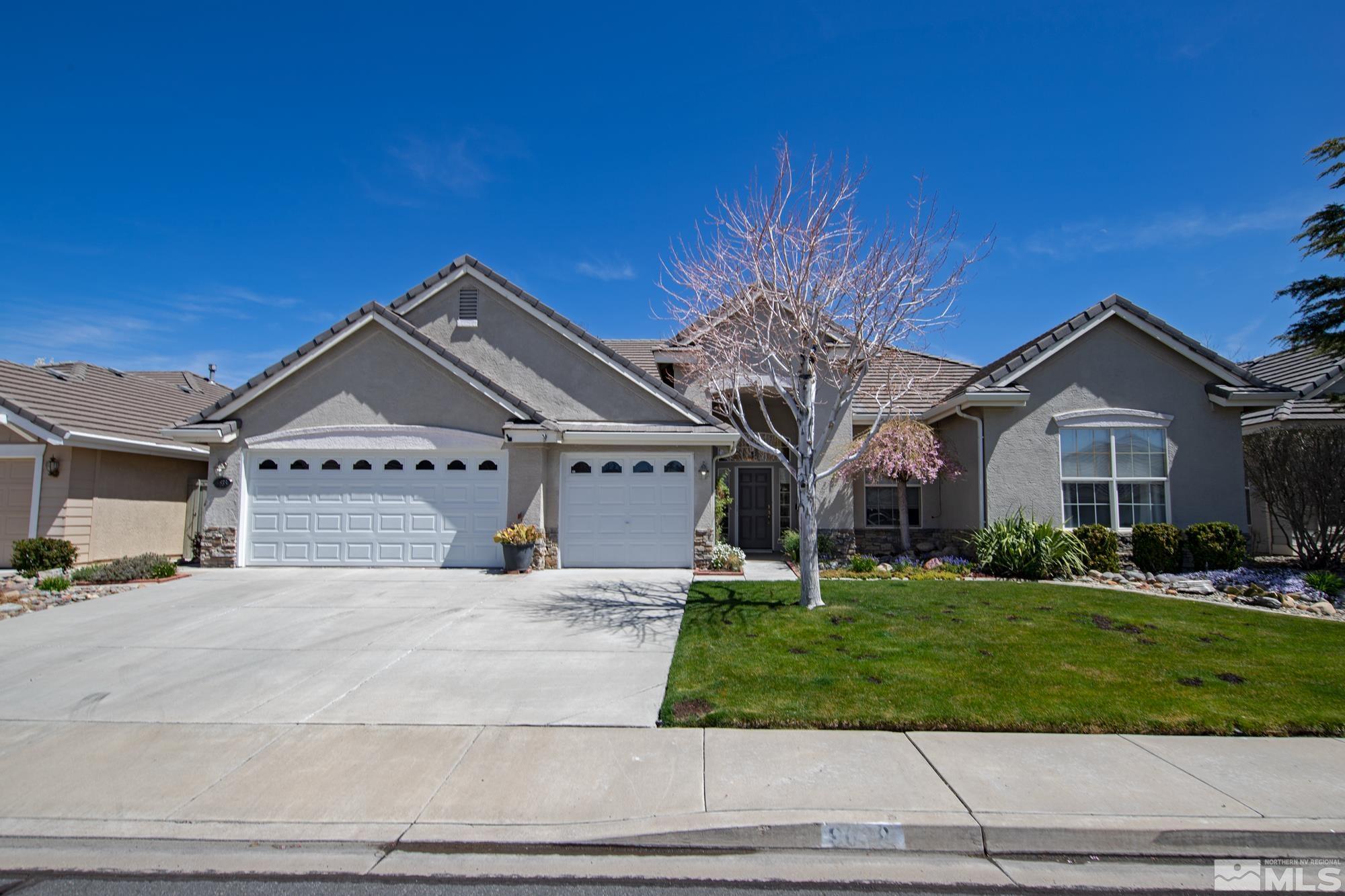 Gray stucco home with two white garage doors, a leafless tree, and landscaped front yard.