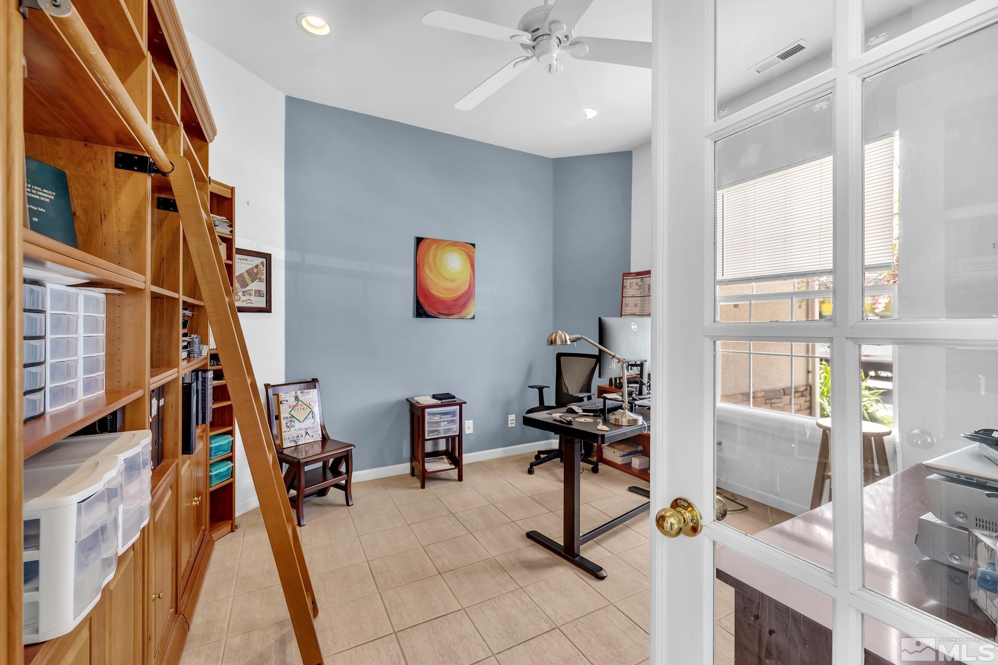 Furnished home office with built-in wooden shelves, rolling ladder, desk, and glass-paneled door.