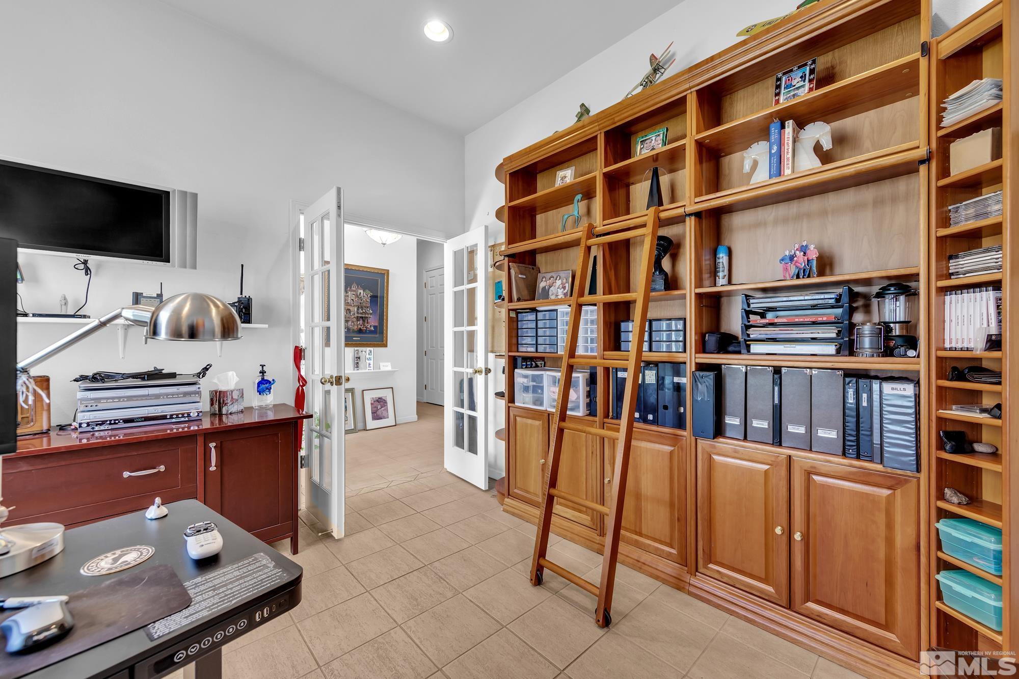 Home office with a wall of wooden shelving and a rolling ladder, desk, and open French doors.
