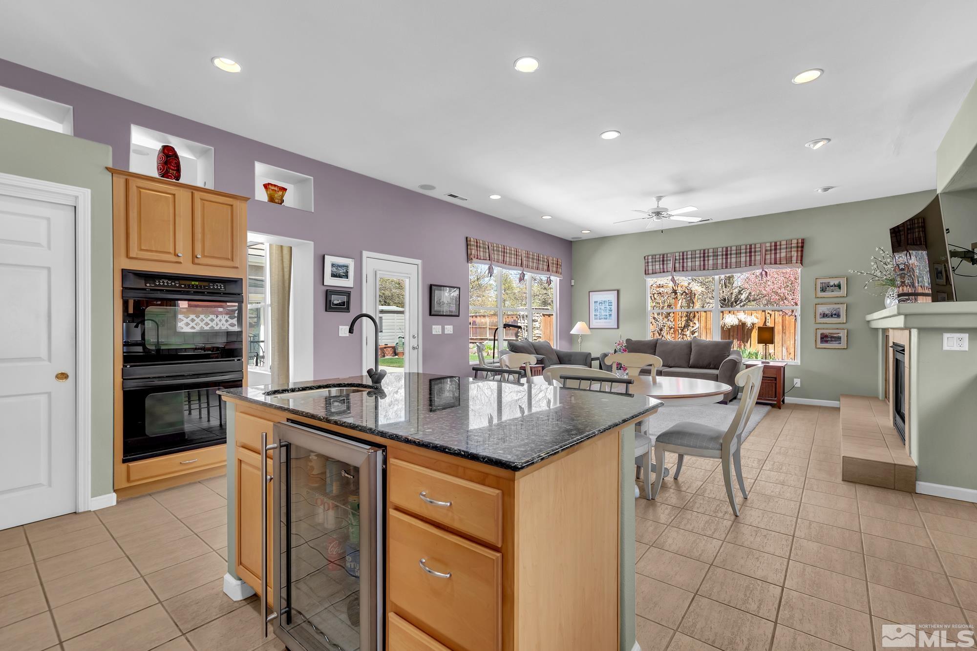 Open kitchen and living area with a granite island, wood cabinetry, and large windows.