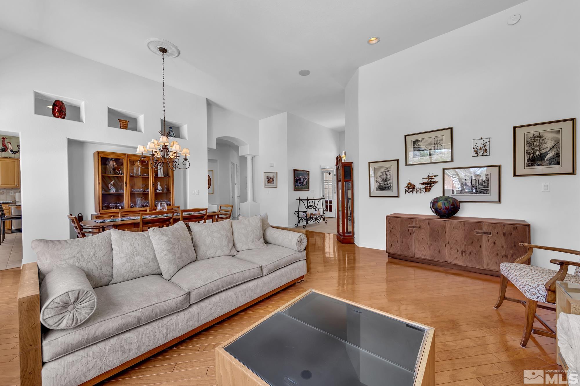 Living and dining area with hardwood floors, a large sofa, chandelier, and maritime artwork.