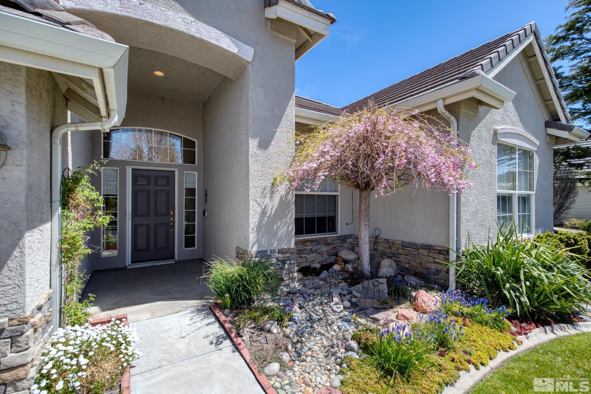 Home entrance with a dark door, stone landscaping, and a flowering pink tree.
