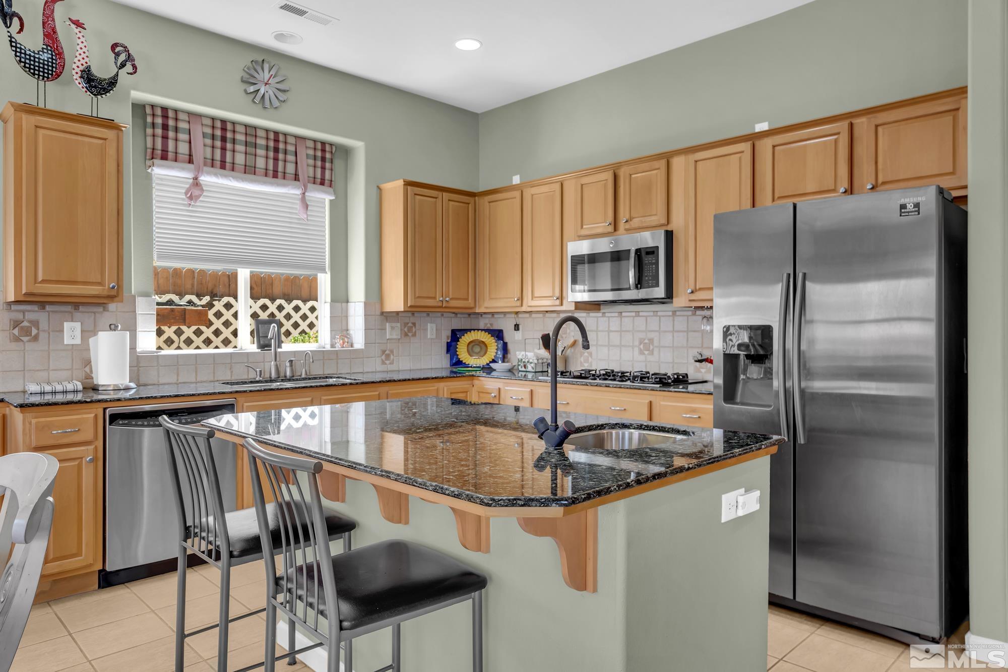 Kitchen with honey-toned cabinets, stainless steel appliances, and a granite breakfast bar with stools.