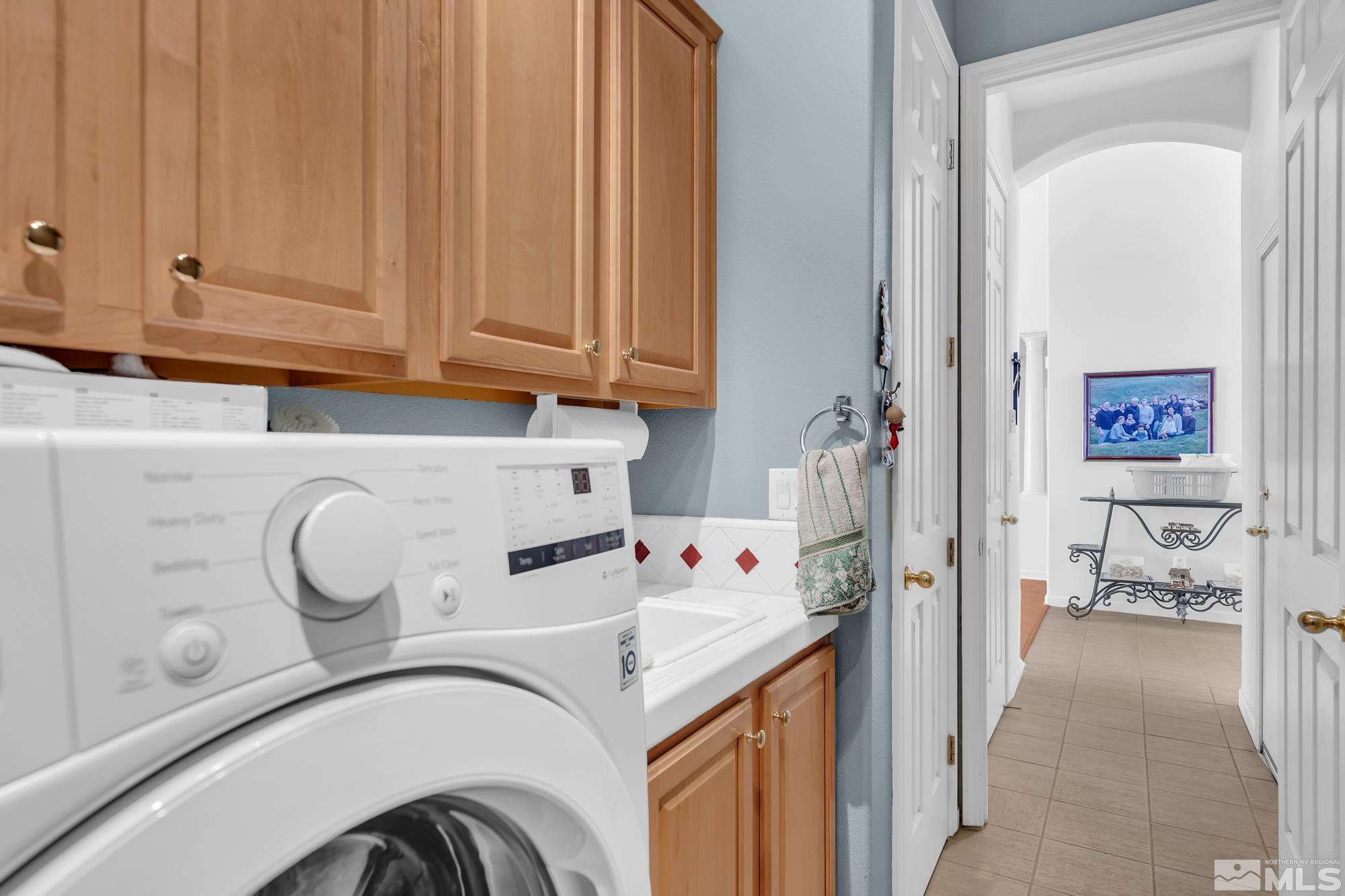 Laundry room with a front-loading washer, utility sink, and wood cabinets beside an open hallway.