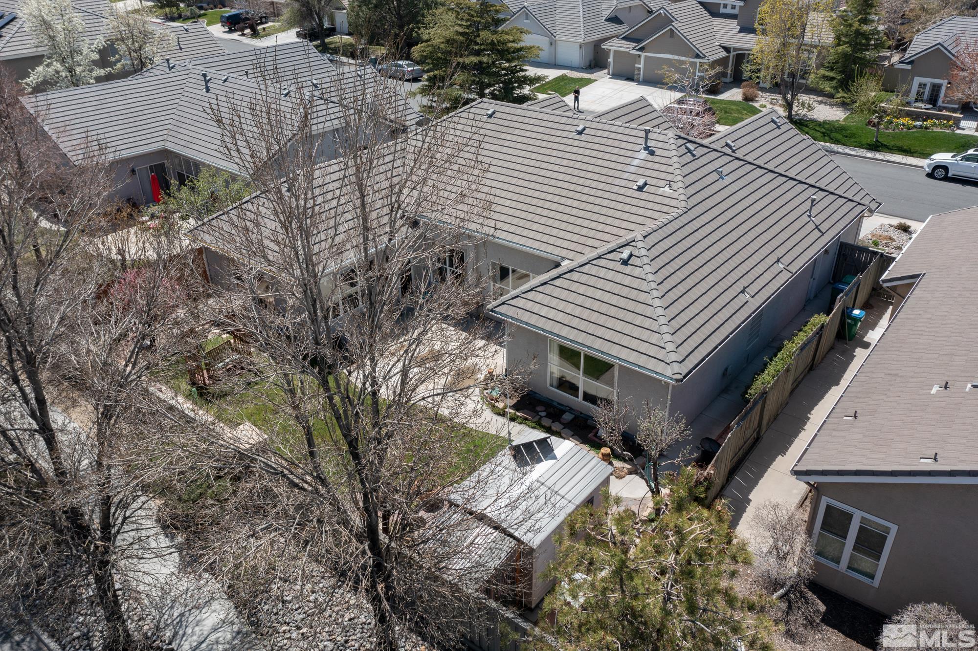 Aerial view of a gray single-story home with a broad tile roof and backyard patio.