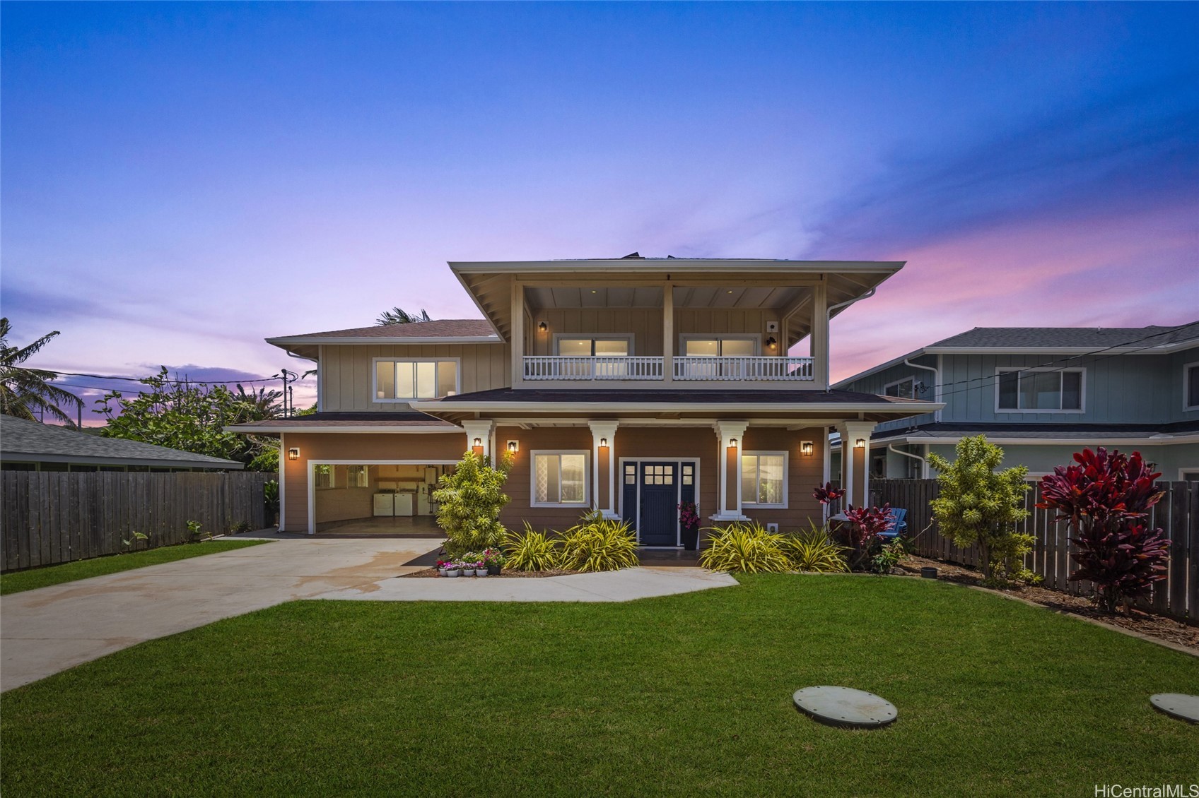 Two-story home with a covered balcony and landscaped lawn at dusk.