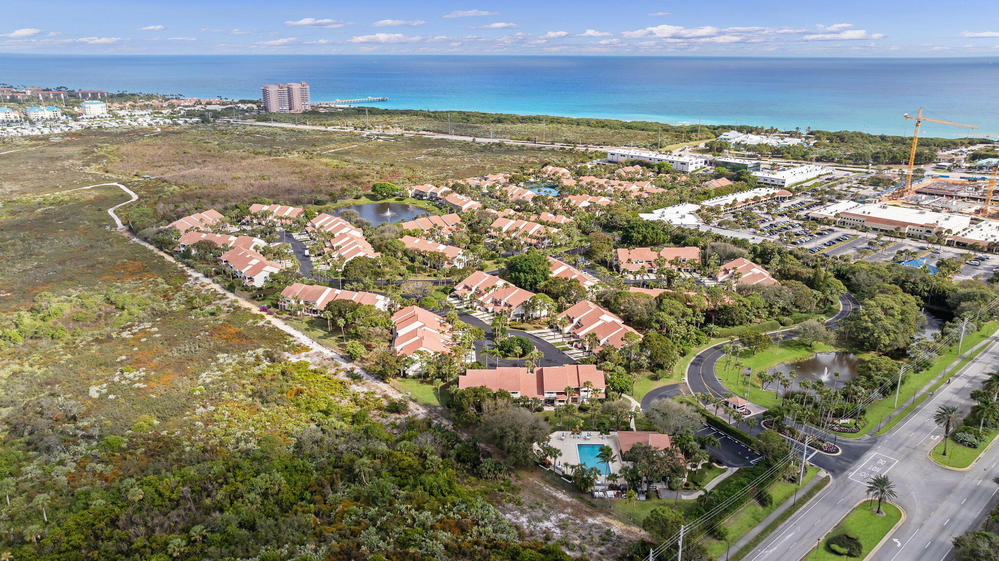 Aerial view of a coastal neighborhood with red-tile-roof homes, wetlands, and ocean beyond.