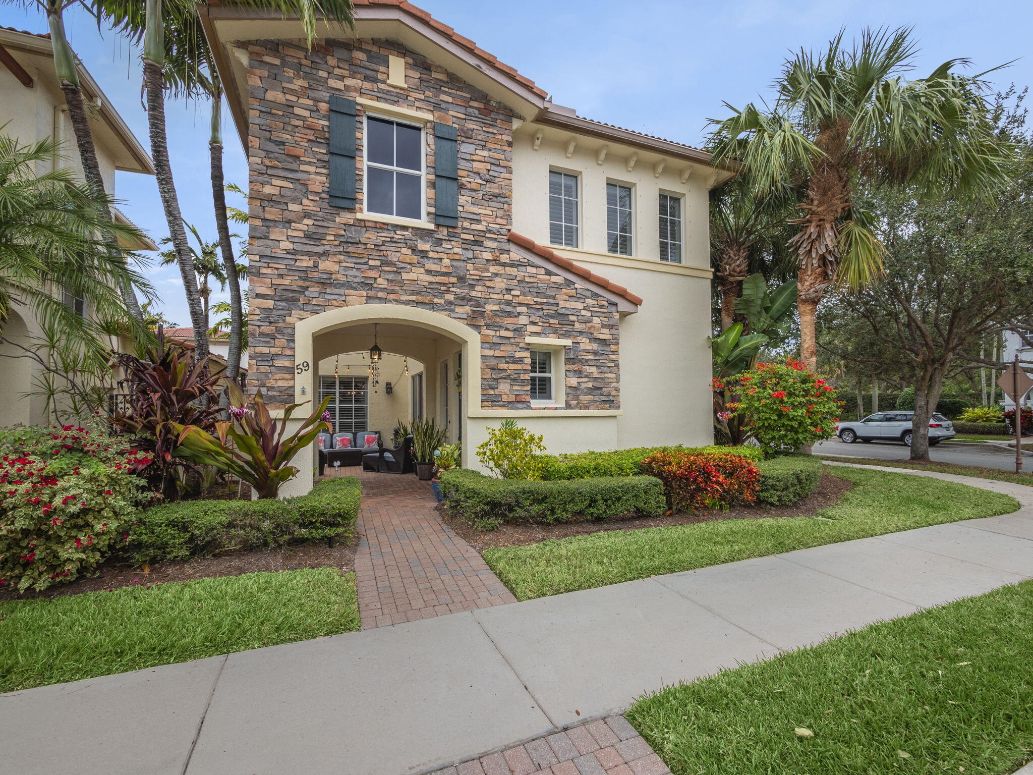 Two-story stone-and-stucco home with an arched entry, brick walkway, and tropical landscaping.