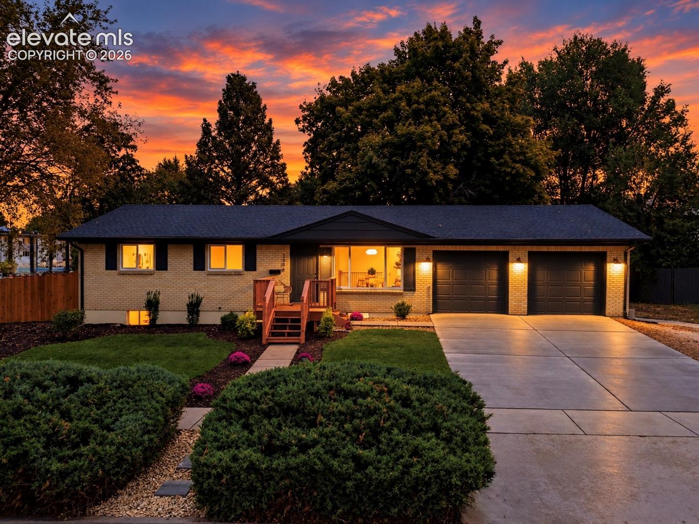 Single-story brick home with two-car garage, landscaped yard, and glowing windows at dusk.