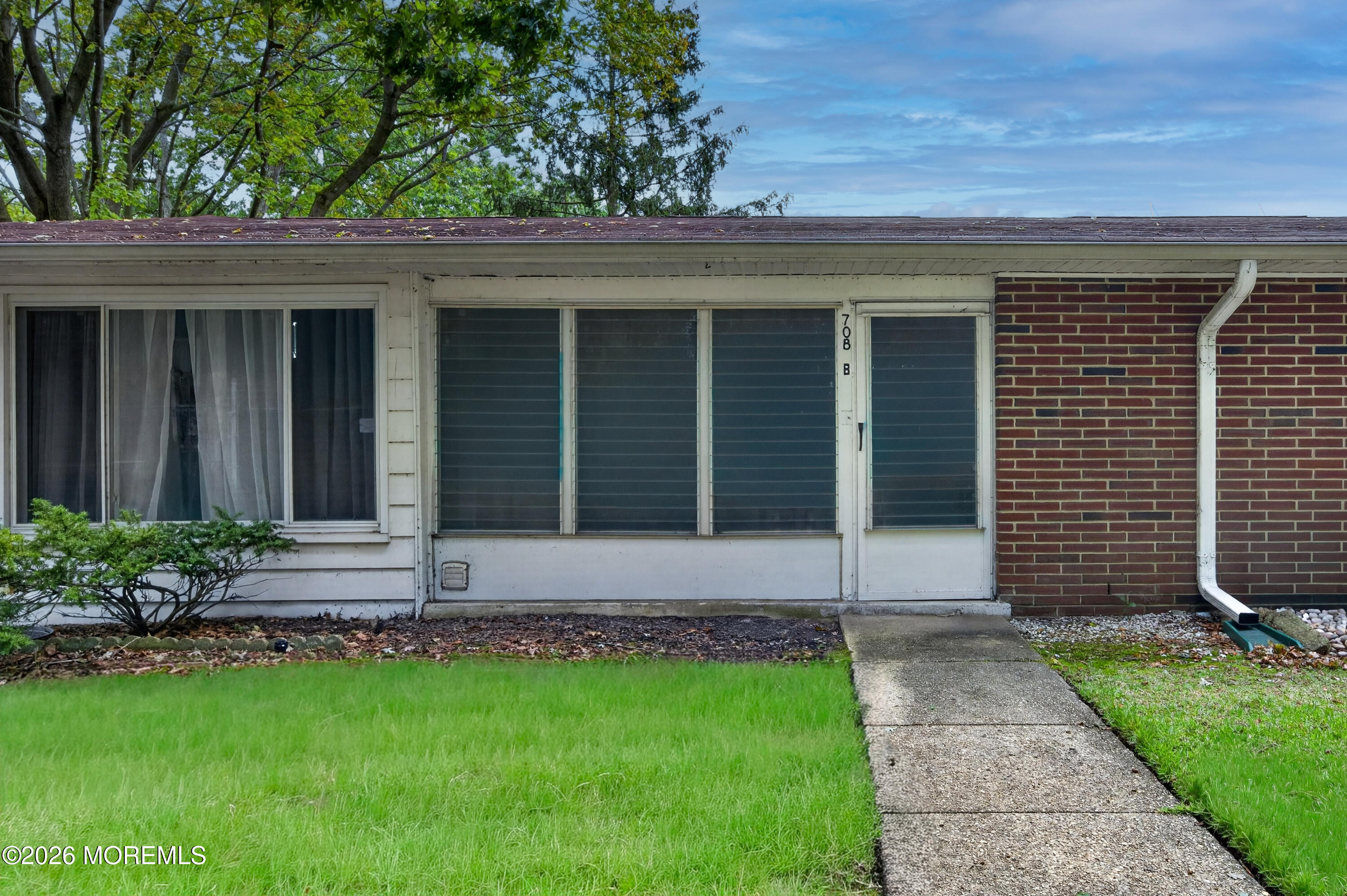 Single-story office exterior with wide windows, a brick section, and a walkway through the lawn.