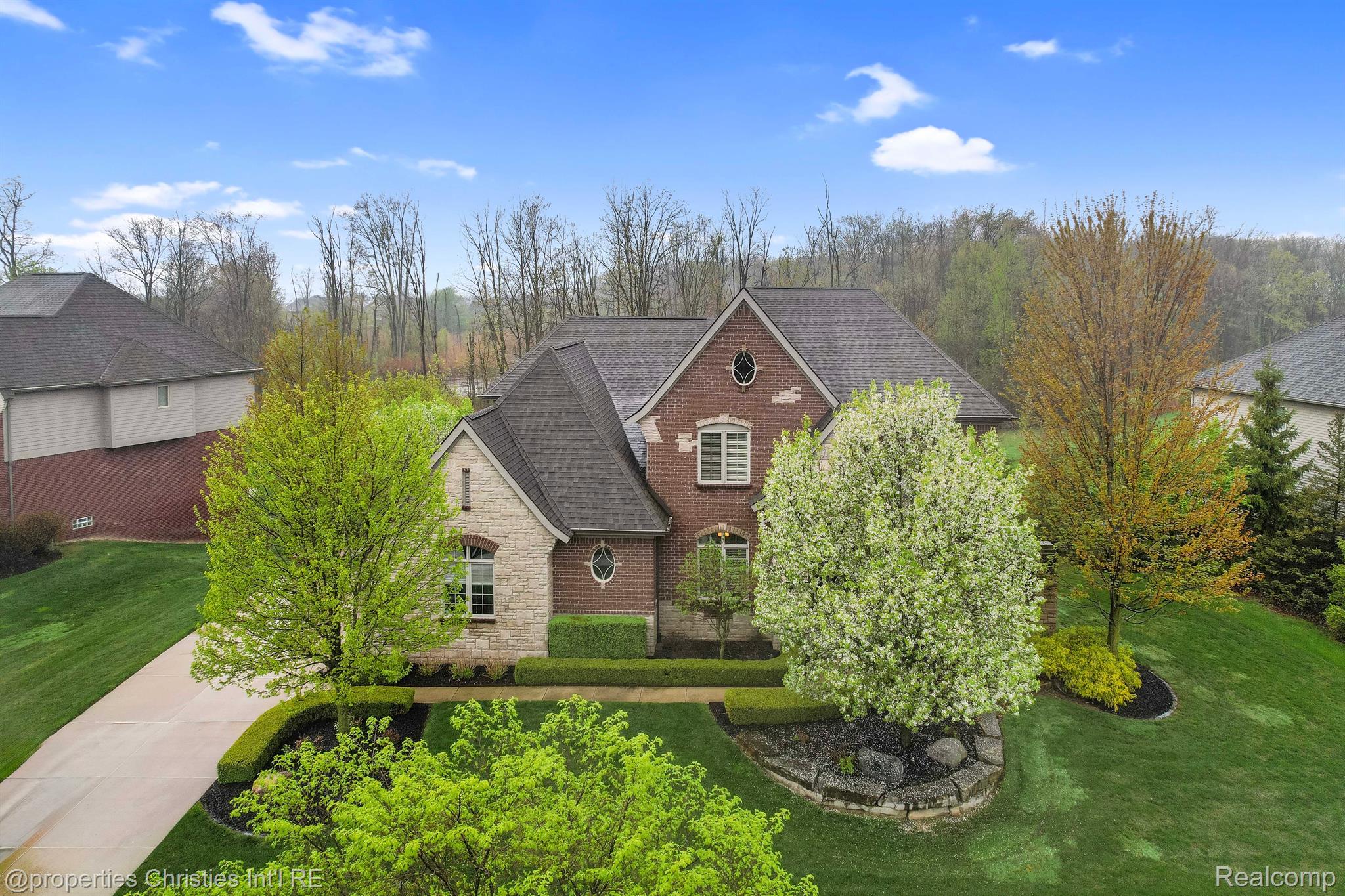 Brick and stone house with flowering trees, landscaped lawn, and a curved driveway.