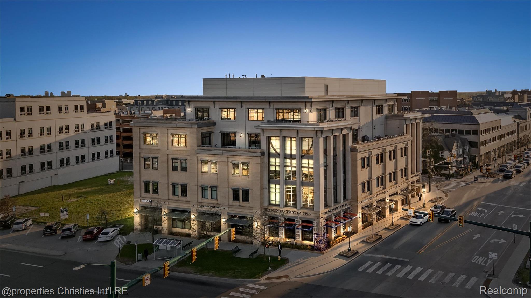 Modern multi-story building with illuminated windows on a city street at dusk.
